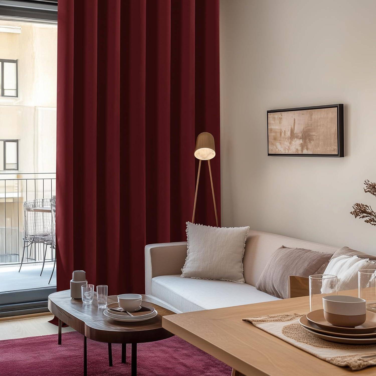 Ein gemütliches Wohnzimmer zeigt ein weißes Sofa, beige Kissen, einen roten Vorhang und einen Holzkaffeetisch mit Tassen. Ein Blick auf den Balkon ist sichtbar.