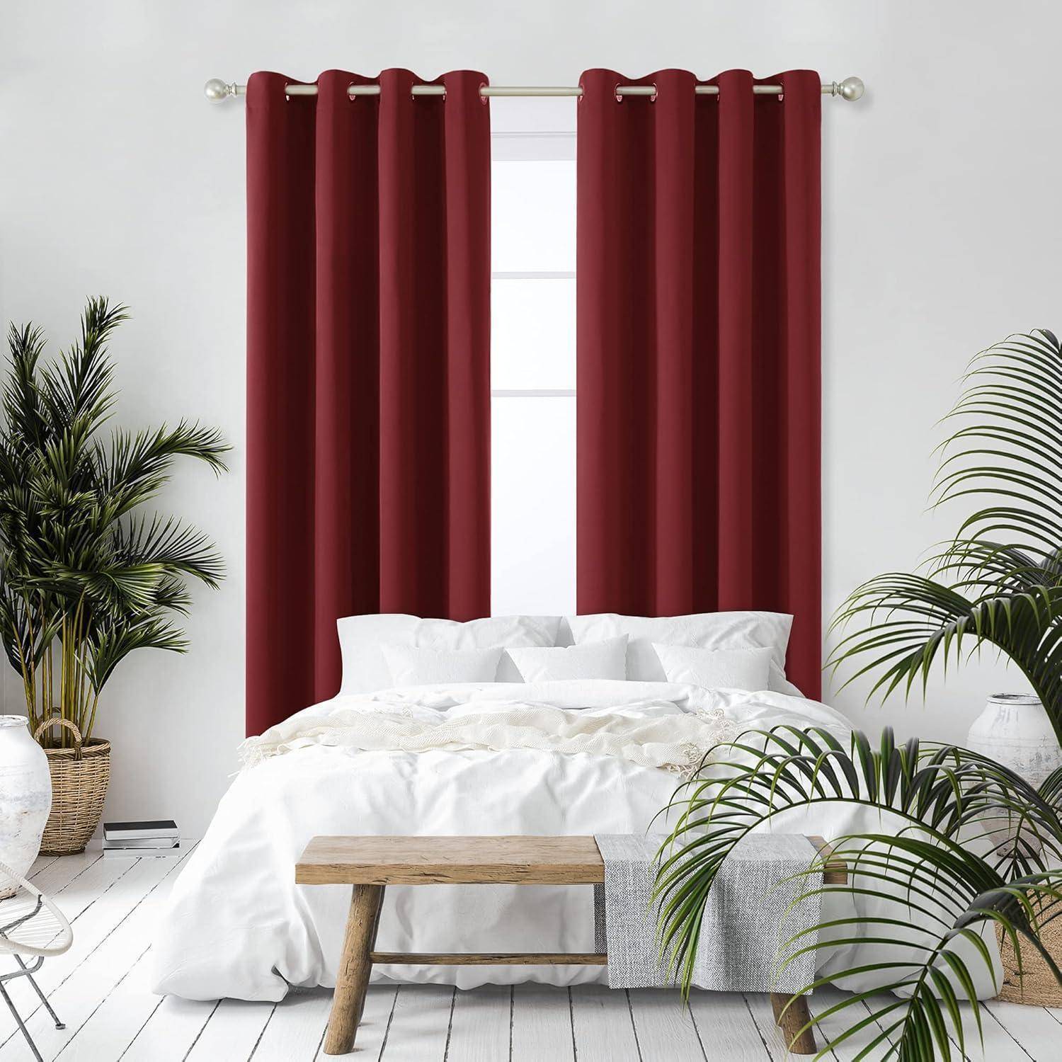Ein sauber gemachtes weißes Bett wird von hohen Topfpflanzen an einer Wand mit roten Vorhängen vor einem Fenster flankiert, wodurch eine gemütliche Schlafzimmeratmosphäre entsteht.