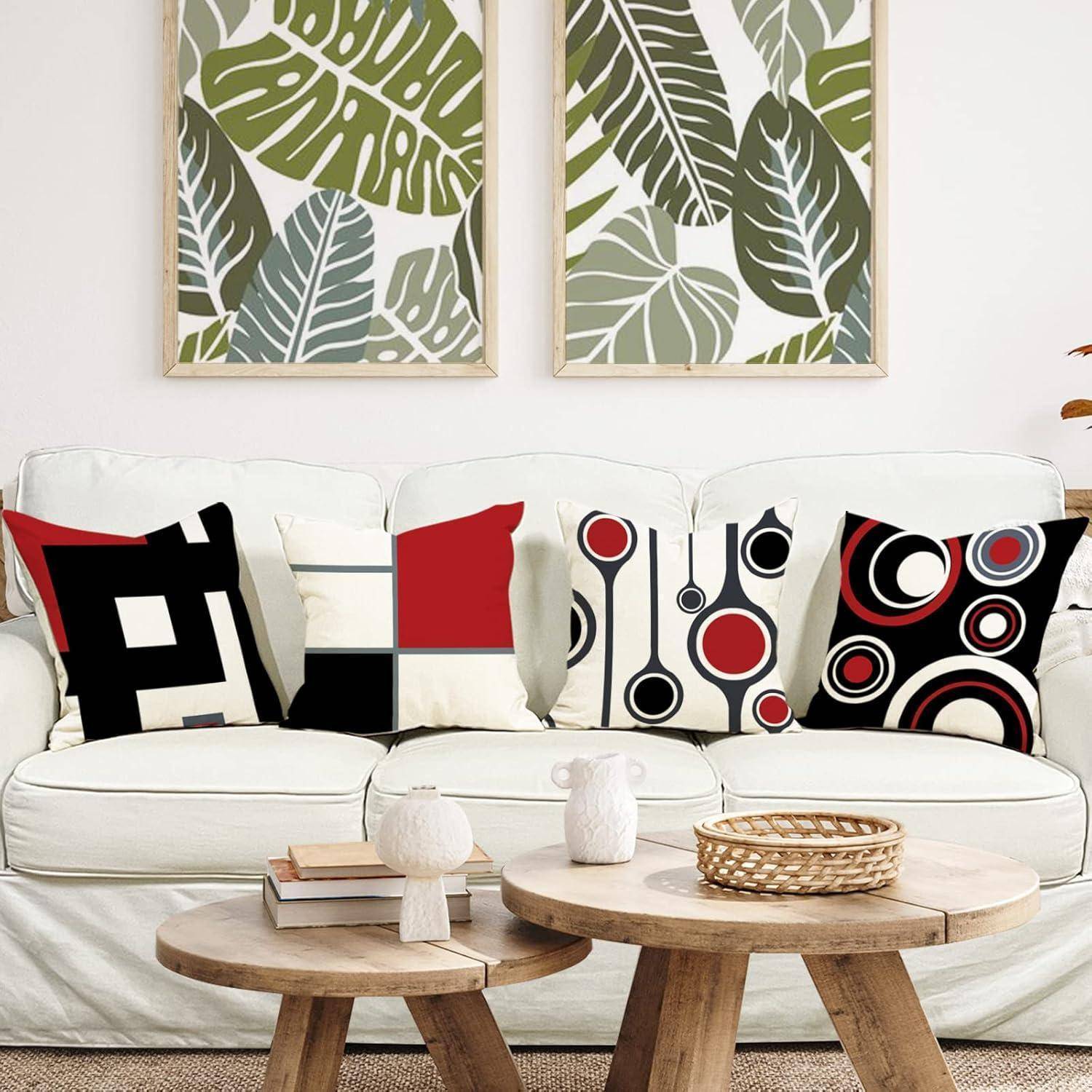 Ein modernes Wohnzimmer mit einem weißen Sofa, das geometrisch gemusterte Kissen trägt, vor einer Wand mit gerahmten tropischen Blätterdrucken.