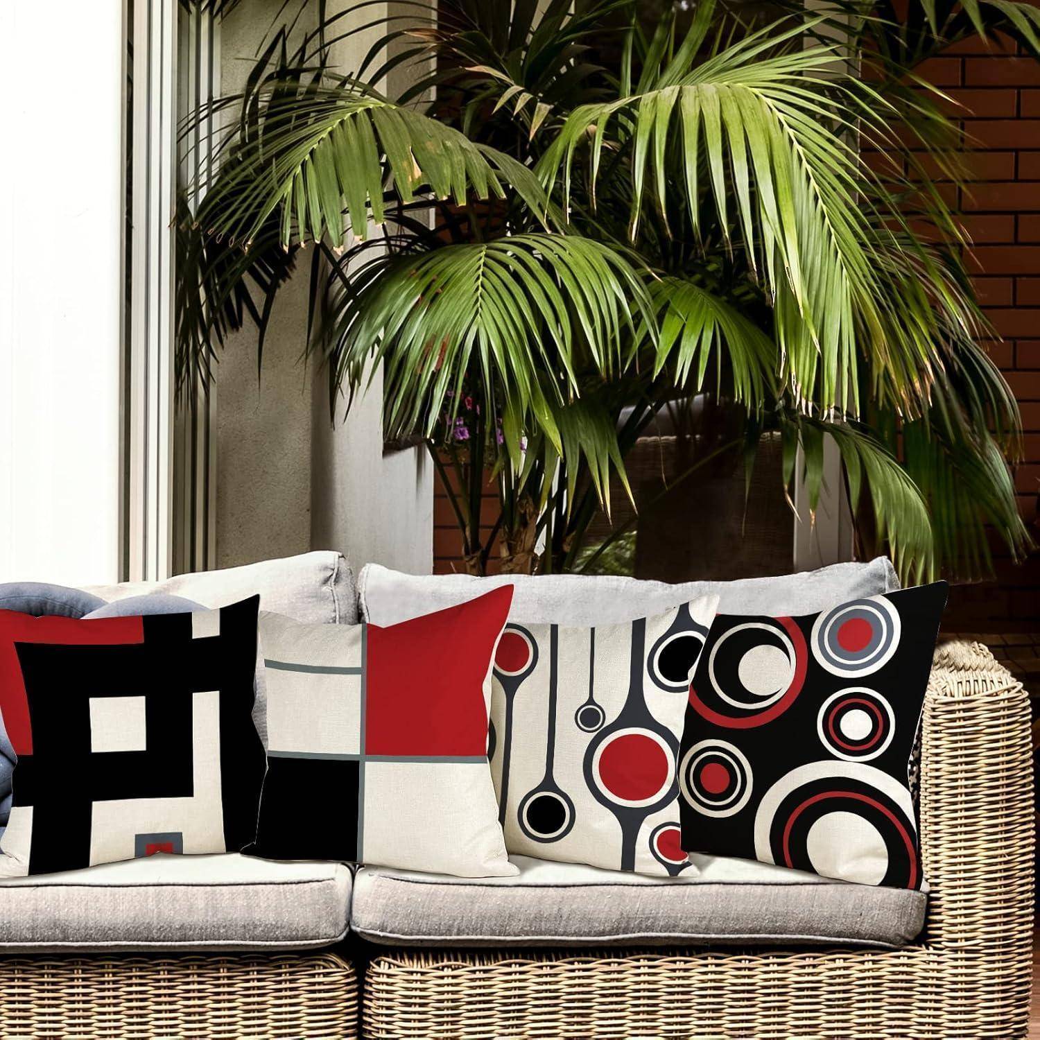 Ein beige Sofa mit vier dekorativen Kissen, die kühne geometrische Muster in Schwarz, Rot und Weiß aufweisen, vor einer Kulisse von grünen Pflanzen.