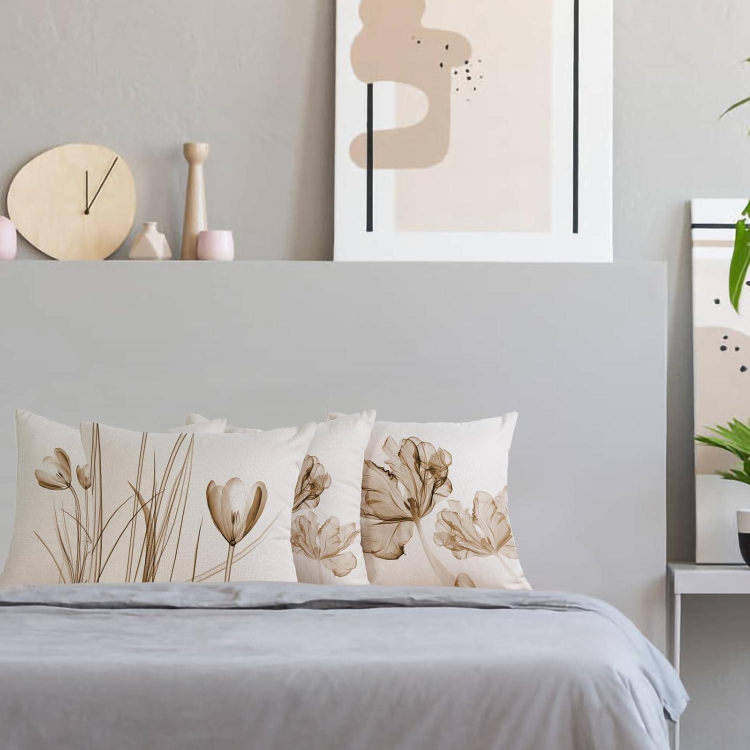 Ein gemütliches Schlafzimmer mit einem grauen Bett, dekorativen Kissen mit Blumendesigns und minimalistischer Kunst und Dekoration an einer hellen Wand.