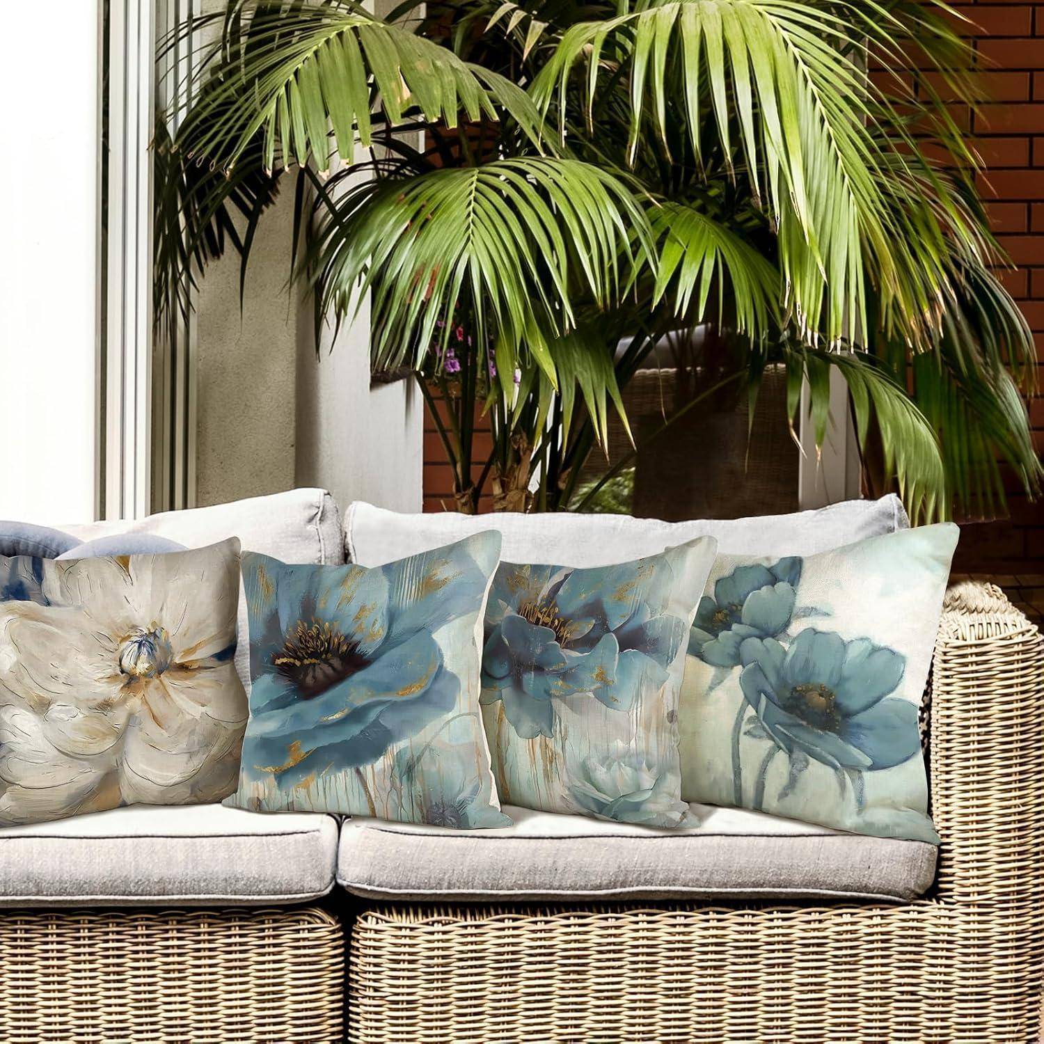 Ein beige Sofa im Freien mit fünf dekorativen Kissen, die blaue und weiße Blumenmotive tragen, vor einer Kulisse üppiger grüner Pflanzen.