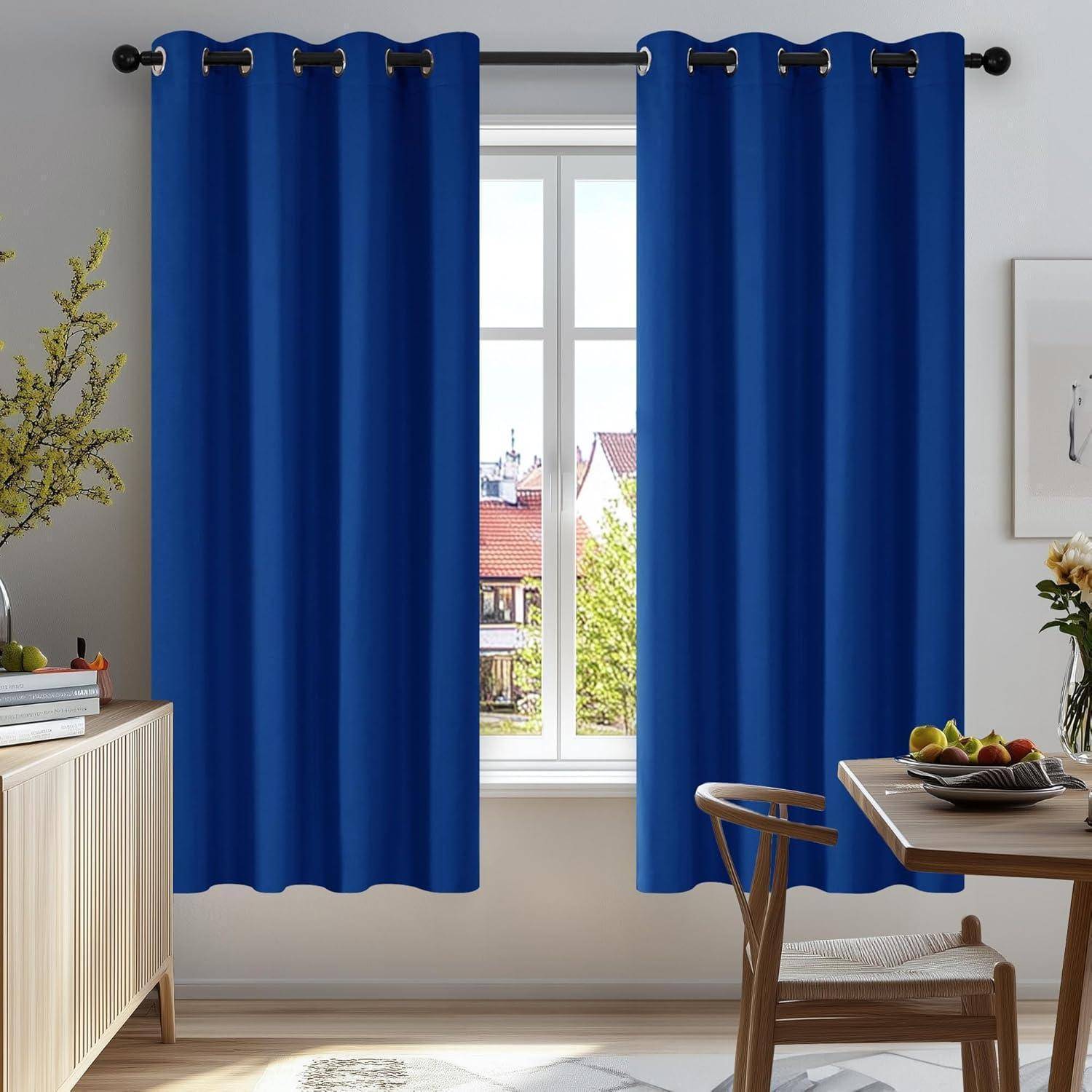 Ein Wohnzimmer mit blauen Vorhängen, die ein Fenster umrahmen und es dem Sonnenlicht ermöglichen, den Raum zu erhellen. Eine kleine Pflanze und ein Wandbild vervollständigen die Dekoration.