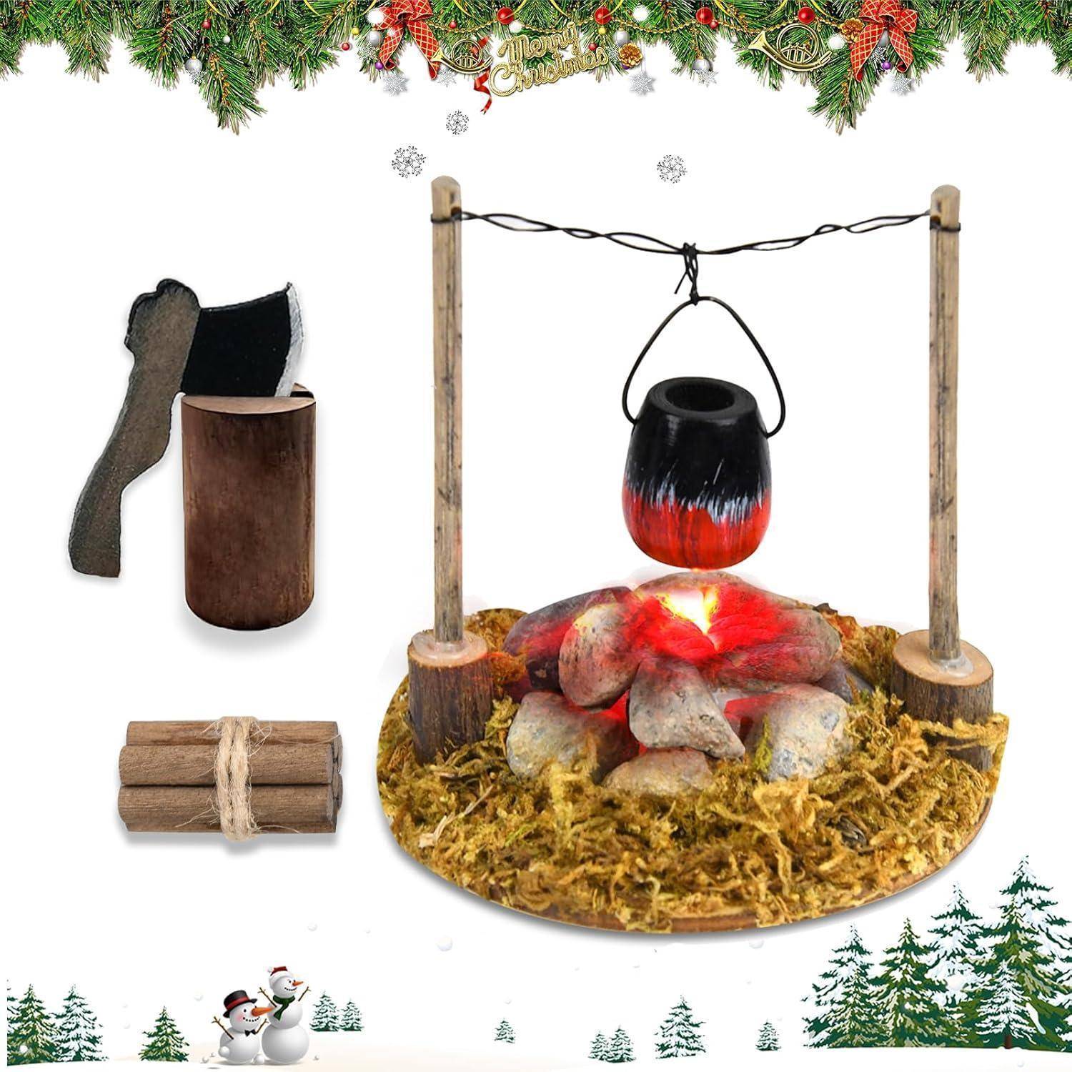 Eine Miniatur-Lagerfeuerszene mit einem Topf, der über Steinen hängt, umgeben von Moos und Baumstämmen. In der Nähe befinden sich eine kleine Axt, ein Holzscheit und ein Bündel Äste.