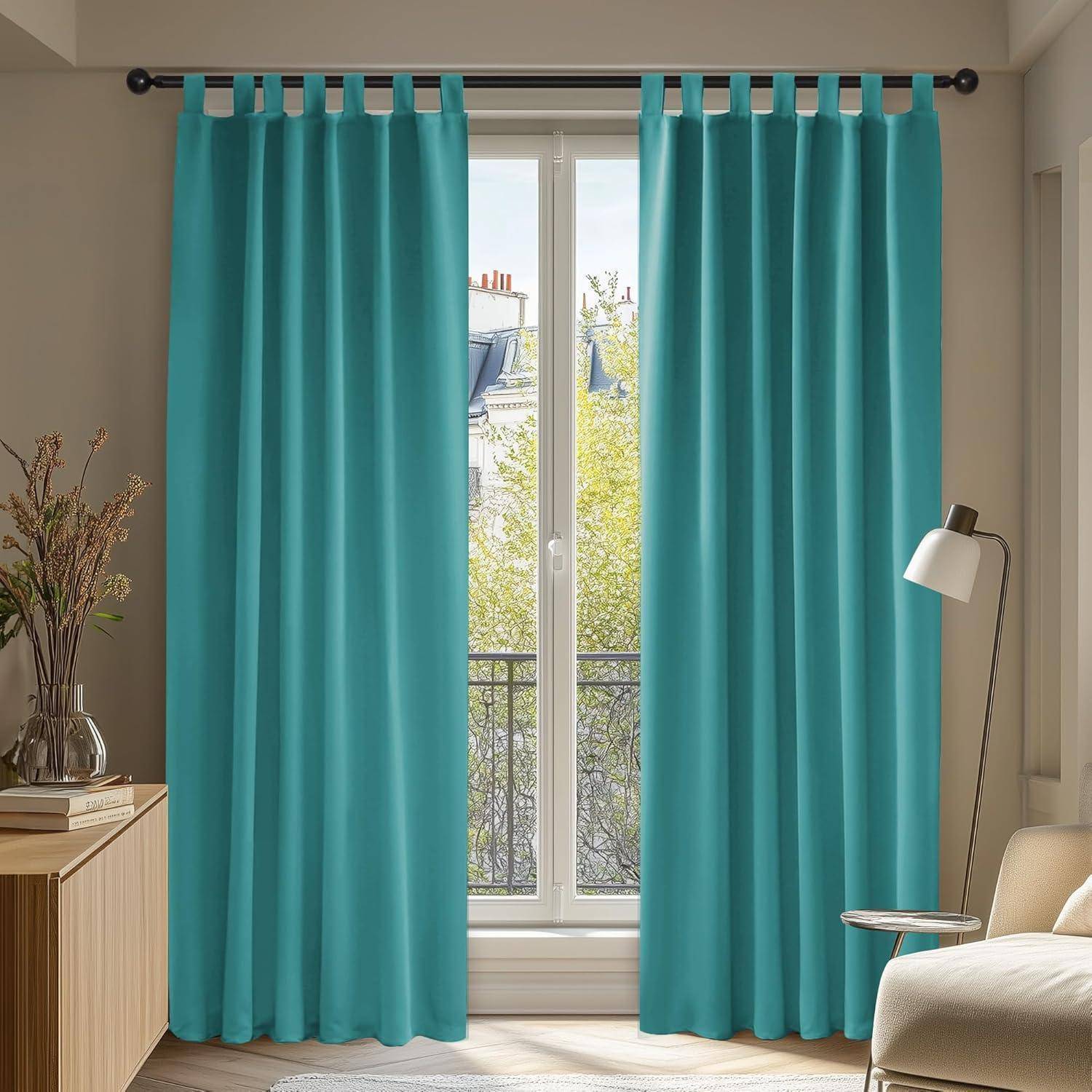 Ein Wohnzimmer mit türkisfarbenen Vorhängen an einem Fenster, die einen Blick auf eine sonnige Stadtlandschaft mit Bäumen freigeben. Eine Lampe und ein Tisch stehen neben den Vorhängen.