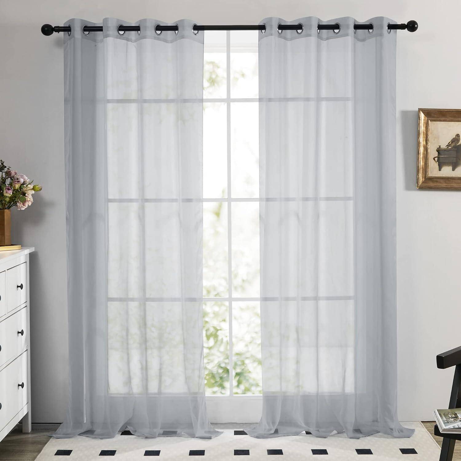 Ein heller Raum mit zarten weißen Vorhängen, die an einem großen Fenster hängen und natürliches Licht durchfiltern lassen. Eine weiße Kommode befindet sich links.