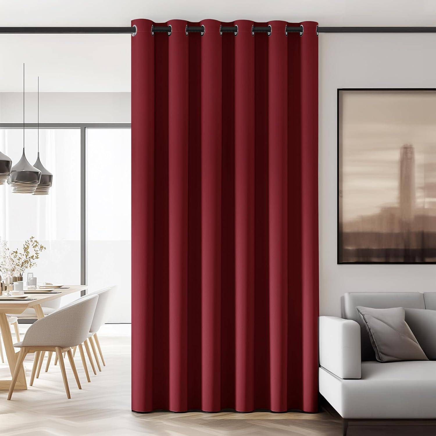 Ein moderner Wohnraum mit einem tiefroten bodenlangen Vorhang, einem weißen Sofa, einem Holz-Esstisch mit Stühlen, Pendelleuchten und Kunst an der Wand.