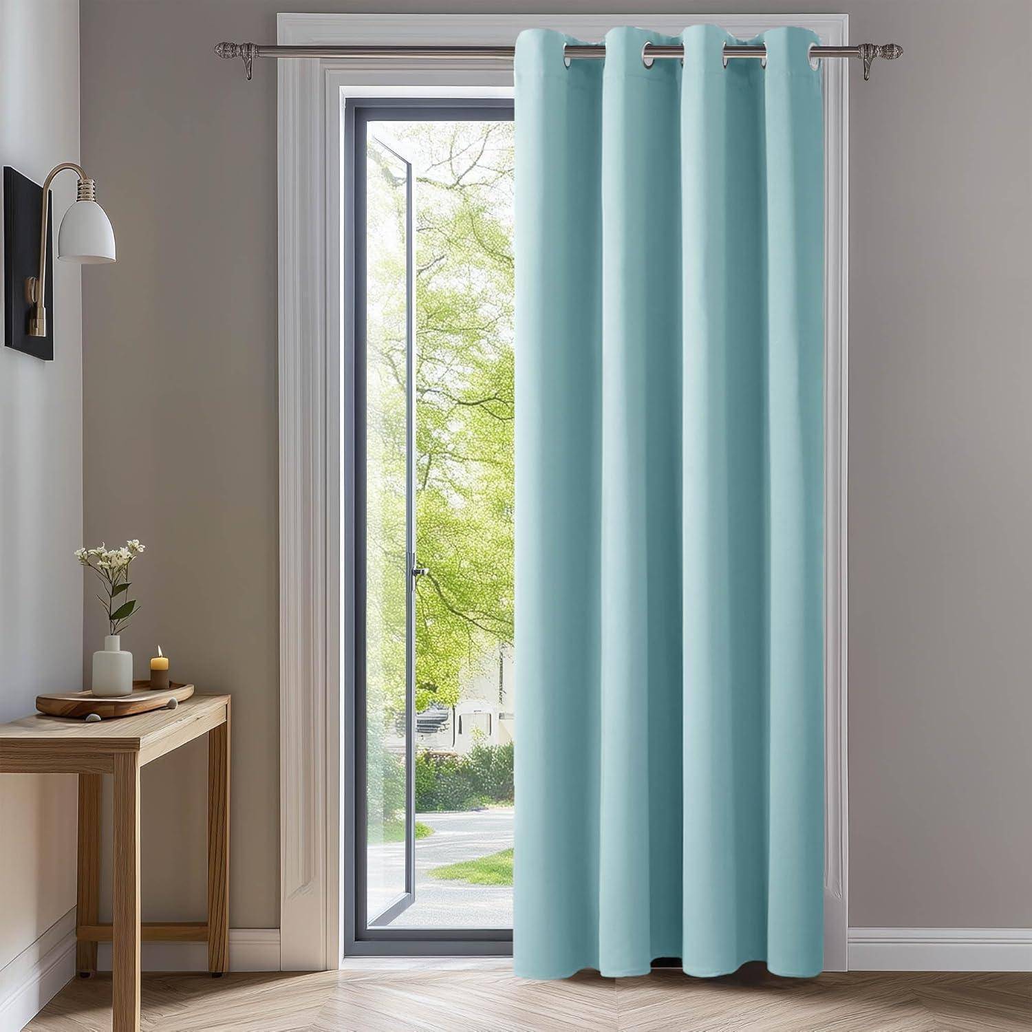 Hellblaue Vorhänge hängen an einem Fenster in einem hellen Raum mit einem kleinen Holztisch, auf dem eine Vase mit Blumen und eine brennende Kerze stehen.