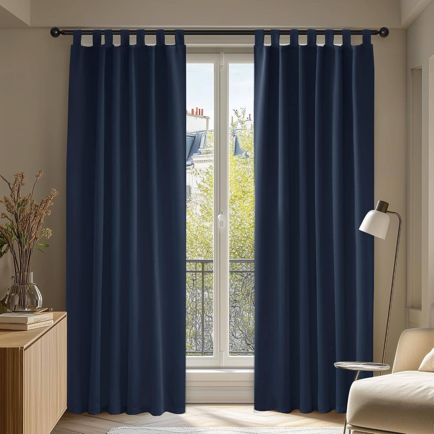 Raum mit großem Fenster, marineblauer Gardine und Stehlampe; Stadtlandschaft und Grünflächen sind draußen sichtbar; Vase mit getrockneten Blumen auf Holzschrank.