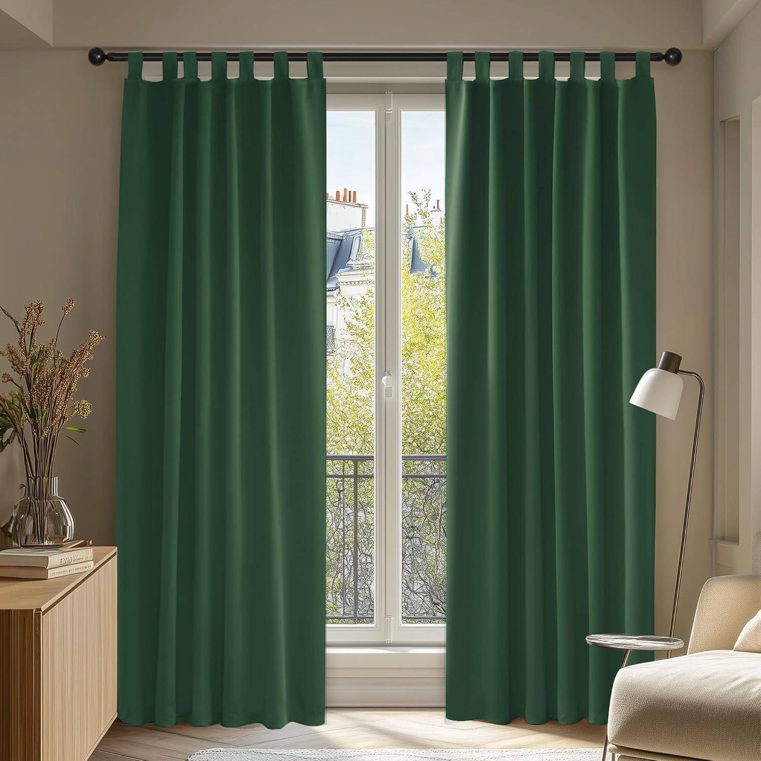 Ein Wohnzimmer mit dunkelgrünen Vorhängen, die ein Fenster verhüllen, einem Holzschrank mit Dekoration auf der linken Seite und einer Stehlampe auf der rechten Seite.