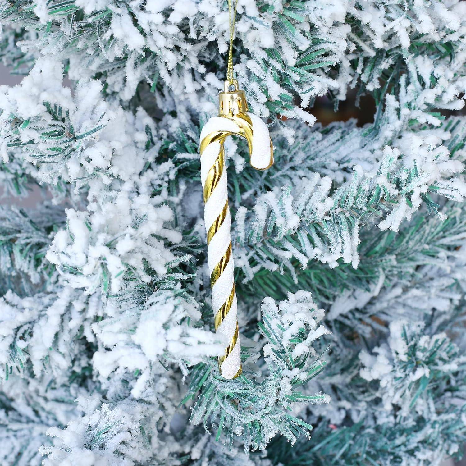 Ein zuckerstagenförmiger Anhänger mit gold- und weißgestreiften Streifen hängt an einem schneebedeckten Zweig eines Weihnachtsbaums.