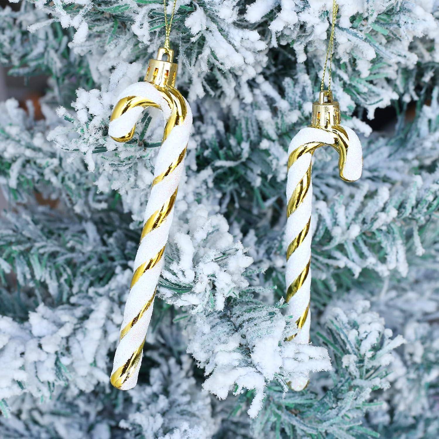 Zwei gold-weiße Zuckerstangen-Christbaumschmuck hängen an einem schneebedeckten Zweig eines Weihnachtsbaums.