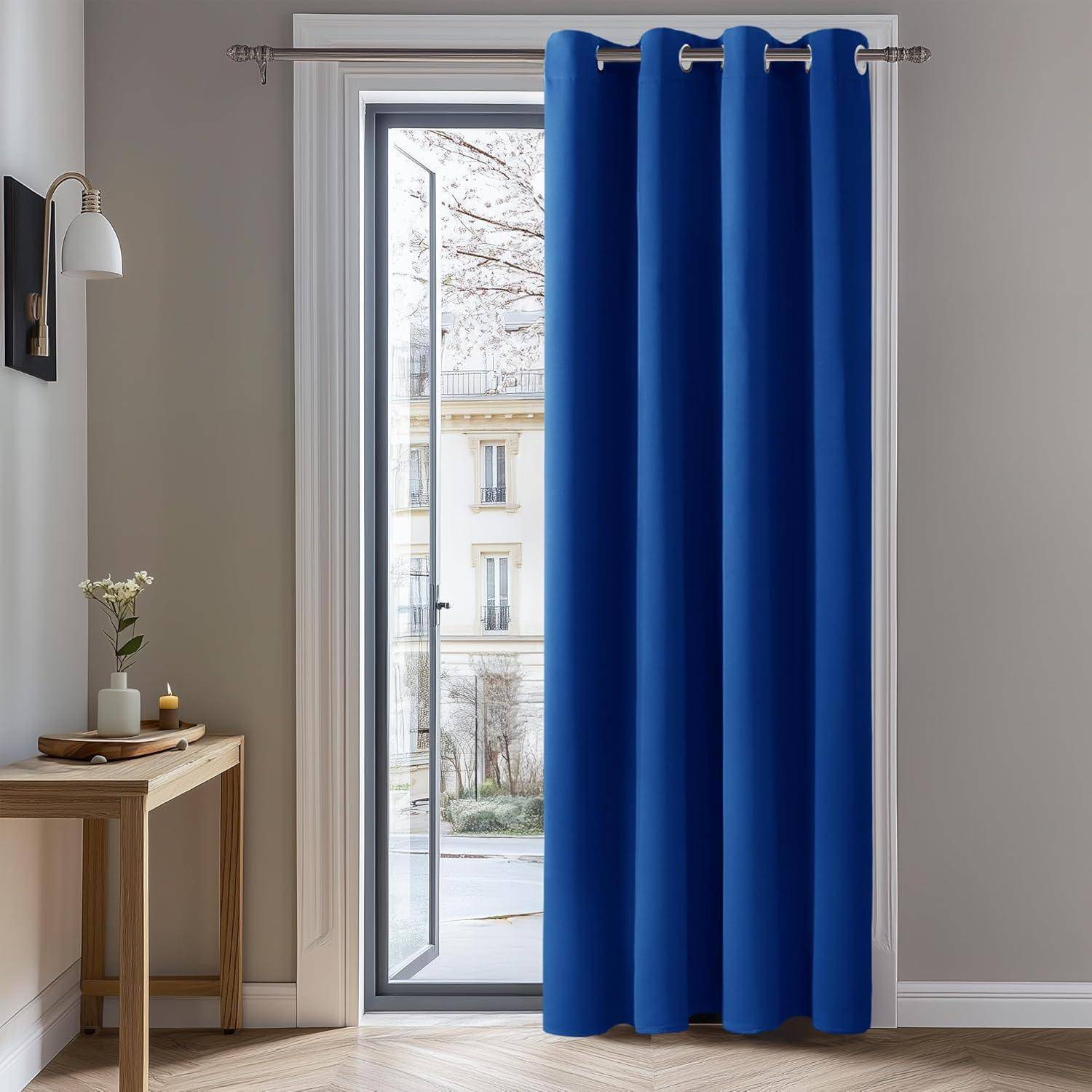 Ein heller Raum mit einem großen Fenster, an dem blaue Gardinen hängen, links ein Holztisch mit einer Vase und Blumen, und ein Blick auf die Straße draußen.