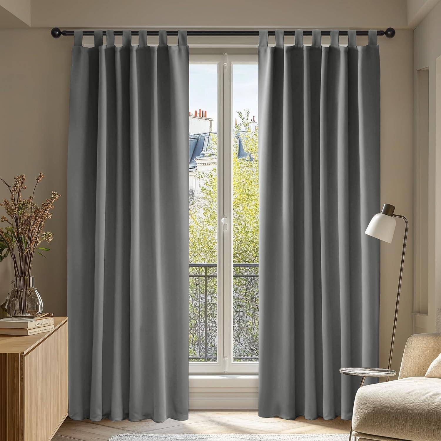 Ein Raum mit grauen Vorhängen, die über einem Fenster zugezogen sind, weiches natürliches Licht fällt hindurch. Eine Stehlampe und ein Holzschrank befinden sich in der Nähe.