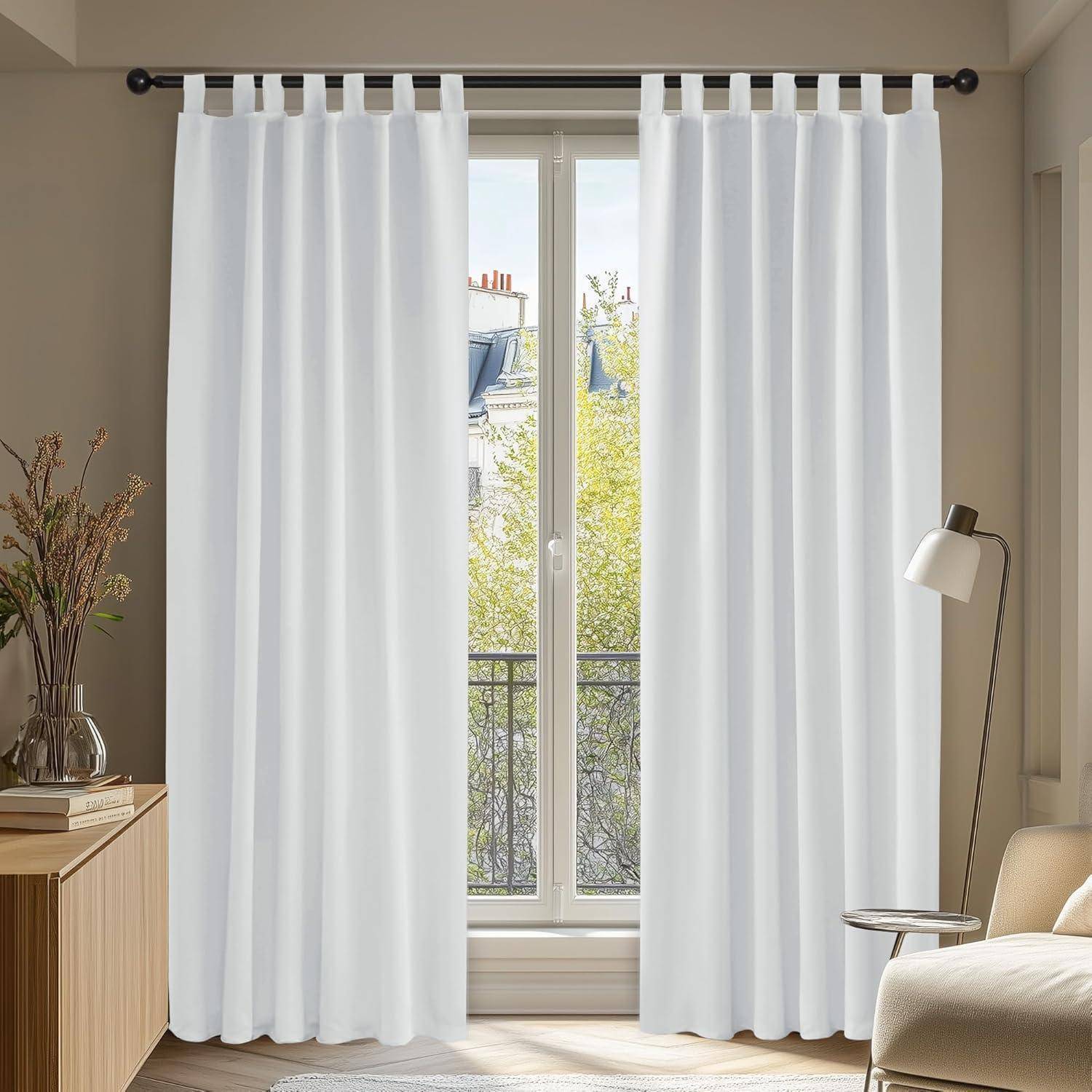 Ein heller Raum mit einem großen Fenster, das von weißen Vorhängen verdeckt wird, ein Holzseitentisch mit einer Vase und Büchern sowie eine moderne Stehlampe.