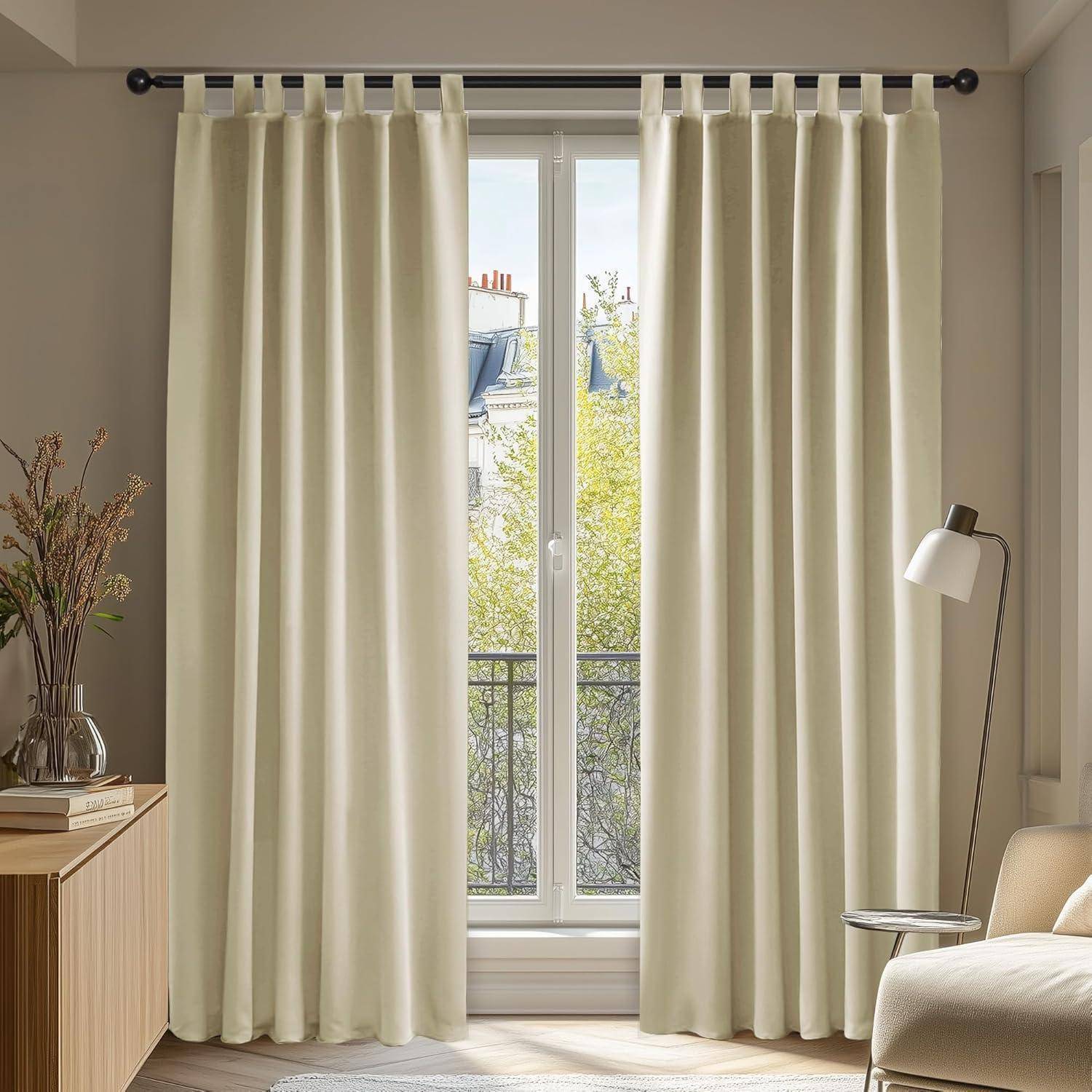 Ein sonnendurchfluteter Raum mit hellbeigen Vorhängen, die ein Fenster umrahmen, durch das ein Baum draußen zu sehen ist. Auf der rechten Seite stehen ein kleiner Tisch und eine Lampe.