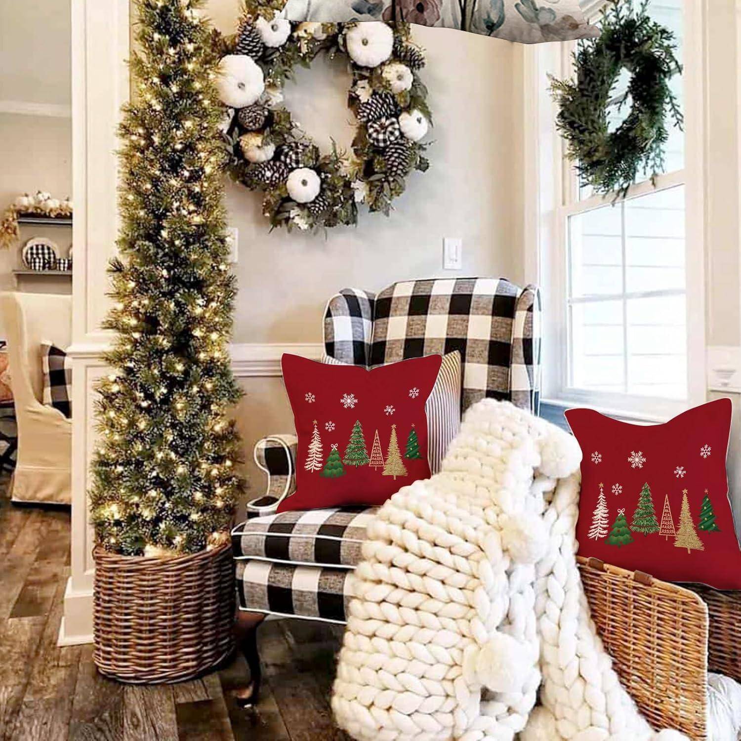 Ein gemütliches Wohnzimmer mit einem karierten Sessel, roten Kissen mit Weihnachtsbaummotiven und einer gestrickten Decke, umgeben von festlichen Kränzen und einem kleinen beleuchteten Weihnachtsbaum.