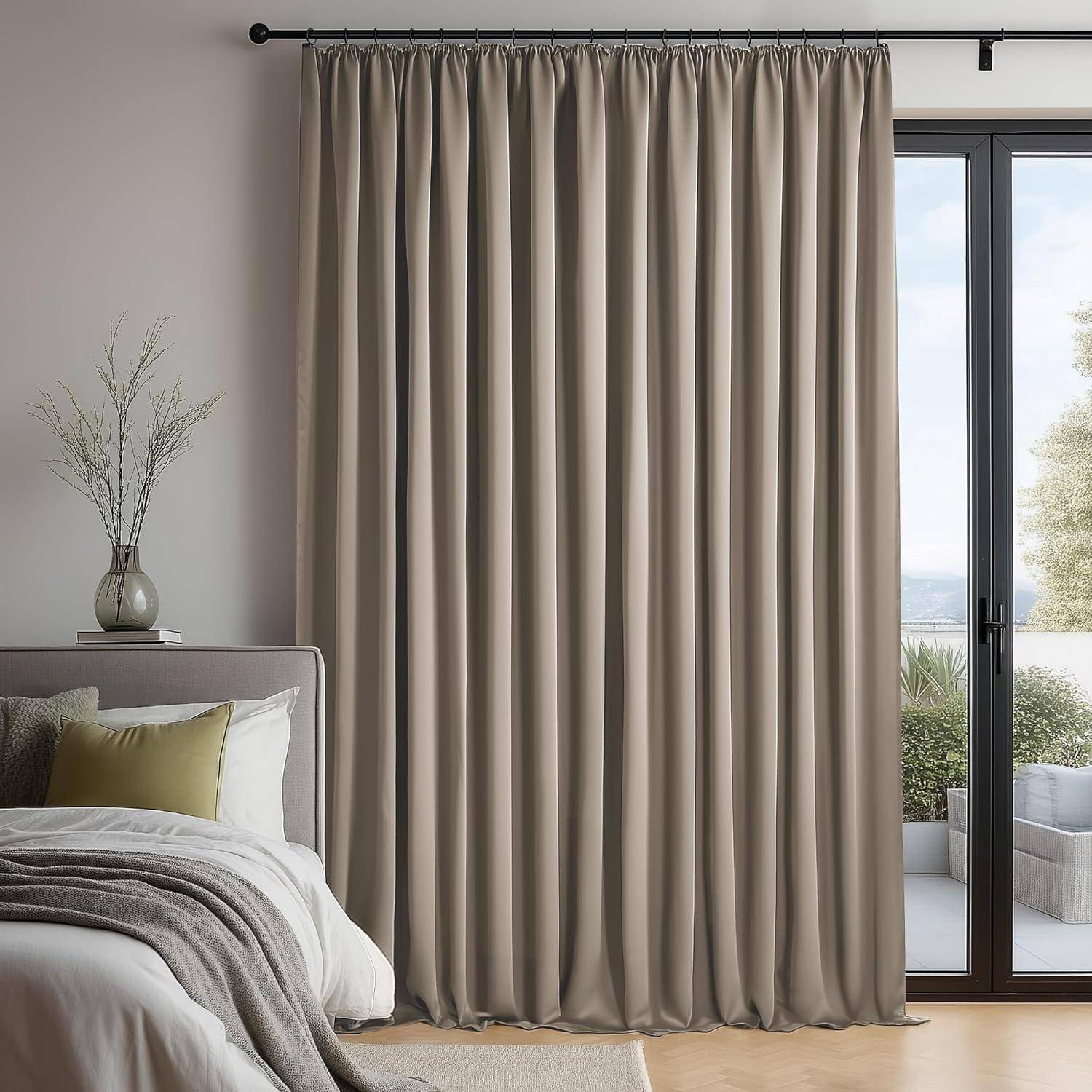 Ein gemütliches Schlafzimmer zeigt ein ordentlich gemachtes Bett, hellgraue Vorhänge, die ein großes Fenster verdecken, und einen Beistelltisch mit einer kleinen Vase mit getrockneten Blumen.