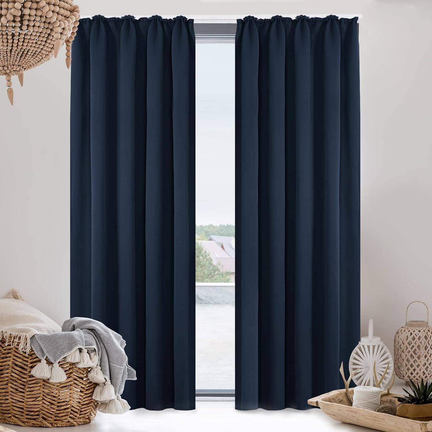 Ein Fenster mit geschlossenen dunkelblau Vorhängen, flankiert von neutraler Dekoration einschließlich eines Korbes mit Decken und einem Keramikblumentopf.