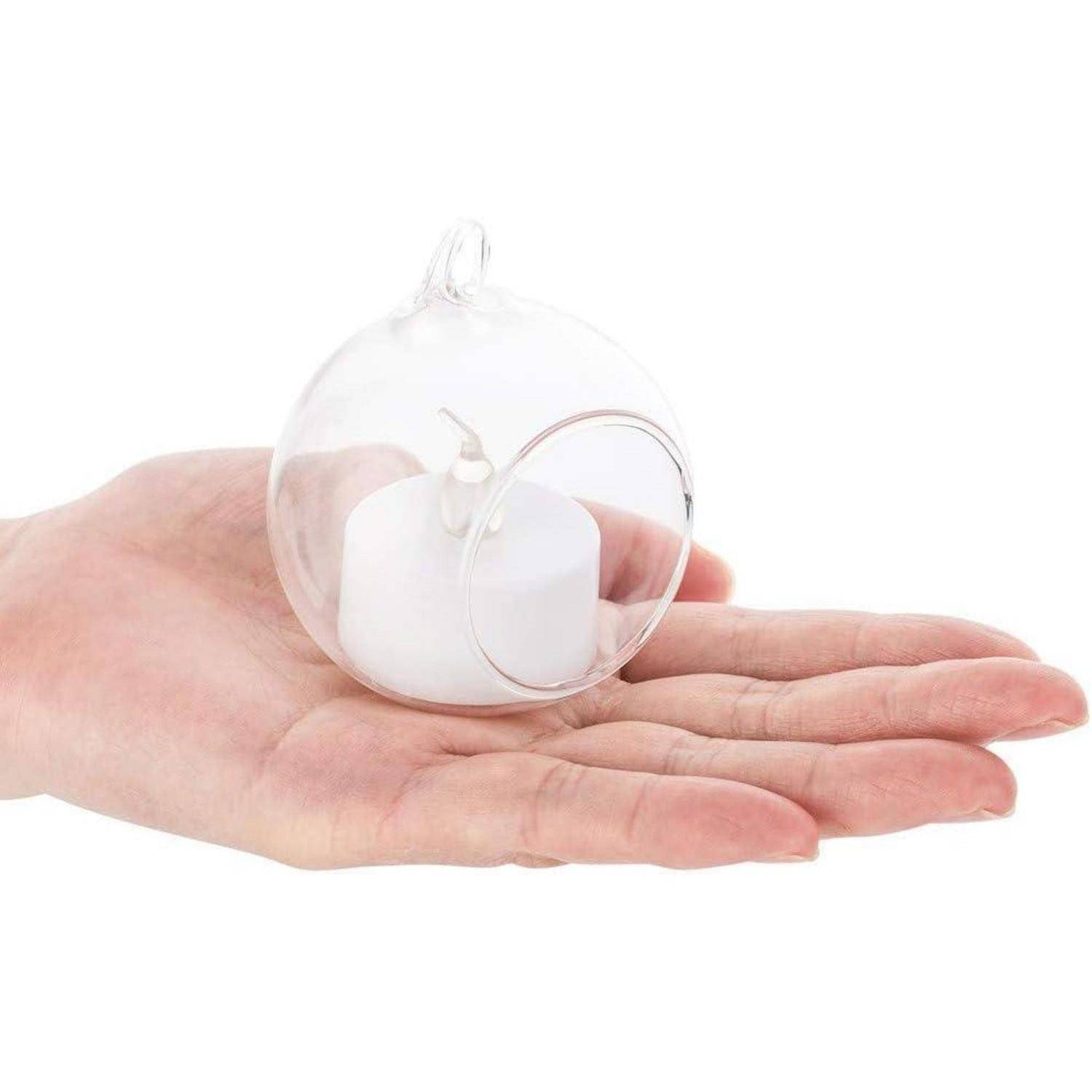 Eine Hand hält eine kleine, durchsichtige Glaskugel mit einer offenen Vorderseite, in der eine weiße Teelichkerze steht, was einen zarten und dekorativen Kerzenhalter veranschaulicht.