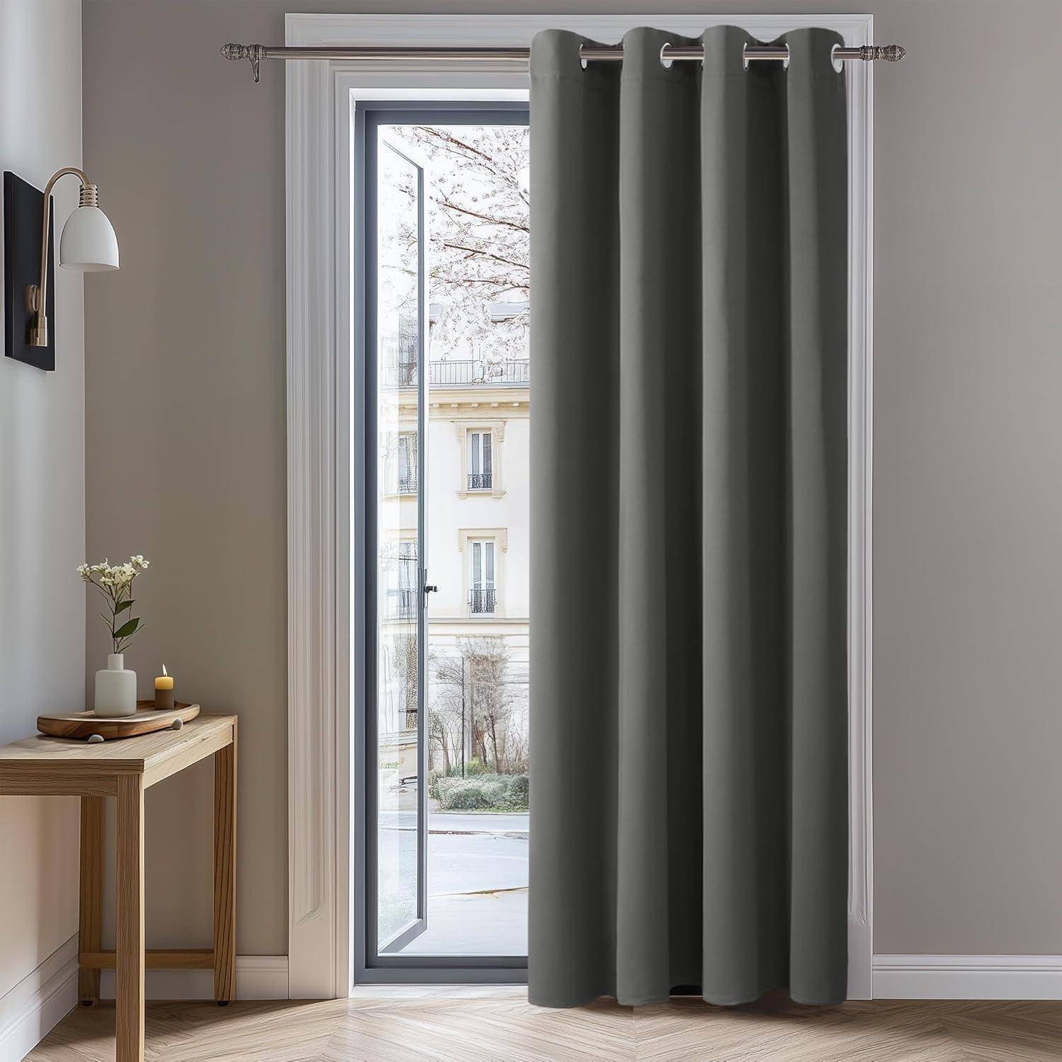Ein Raum mit einem Holztisch, einer Vase mit Blumen und einem schwarzen Vorhang, der ein hohes Fenster mit Blick nach draußen verdeckt.