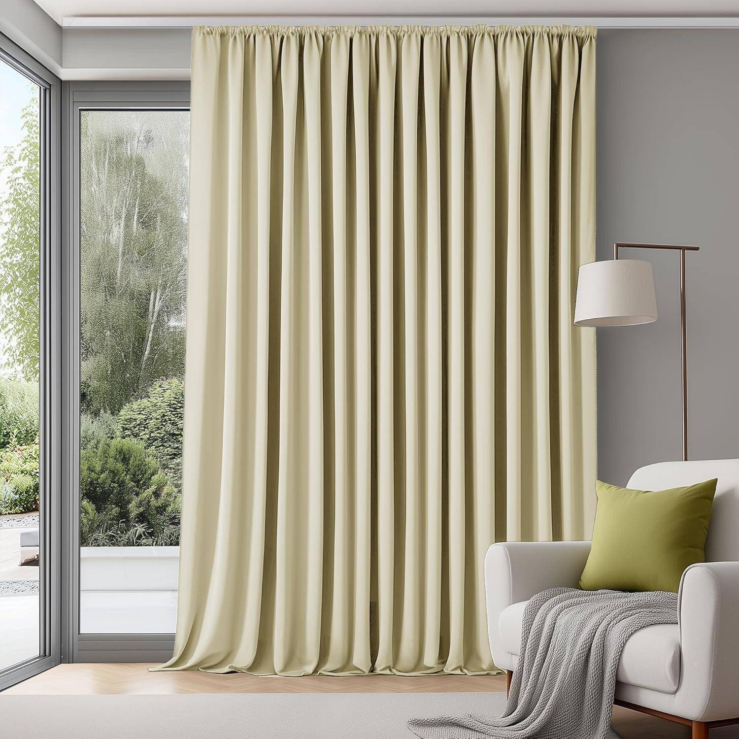 Eine gemütliche Ecke im Wohnzimmer mit einem Sessel, grünem Kissen, weißer Lampe und bodenlangen beigen Vorhängen neben einem großen Fenster mit Blick auf Grünflächen.