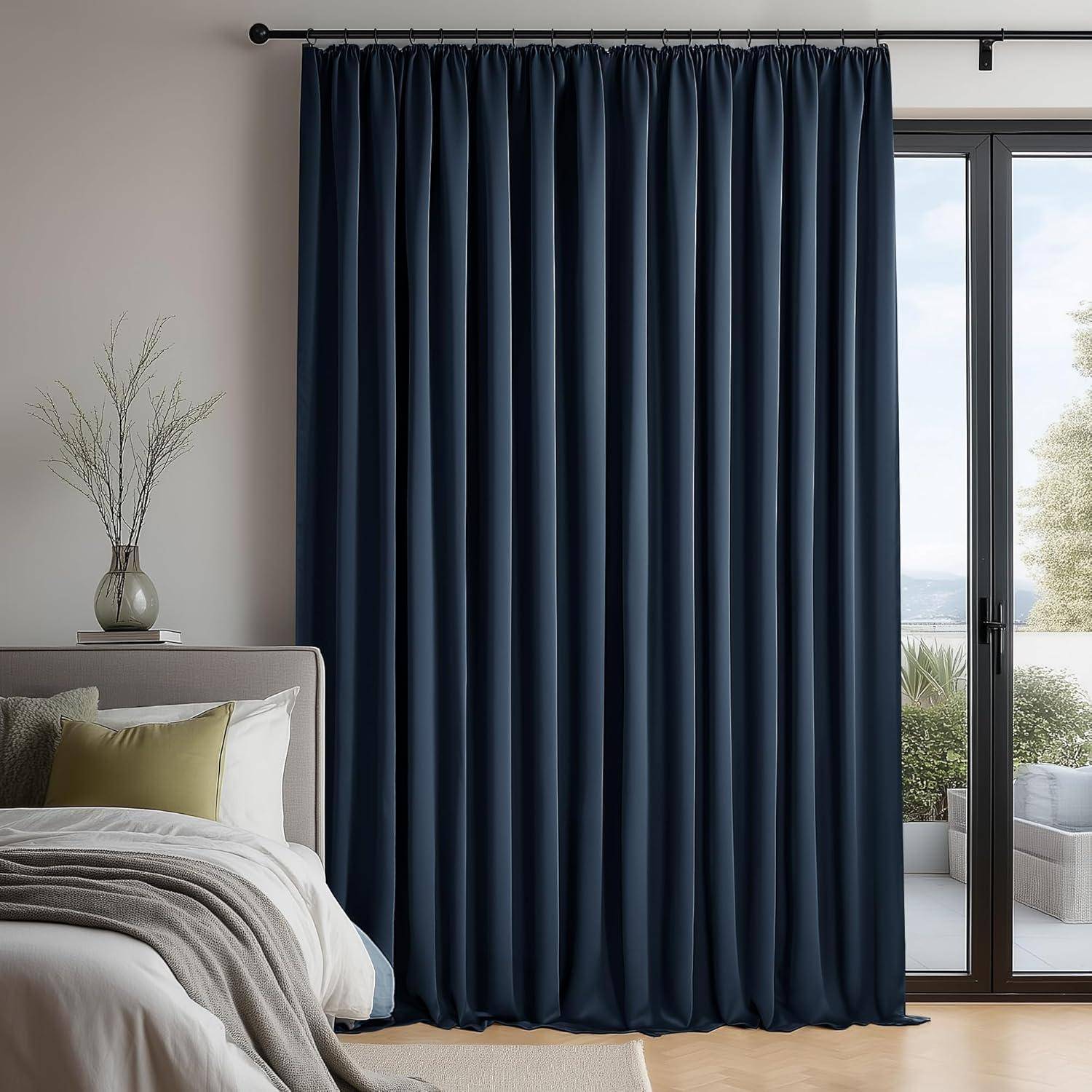 Ein Schlafzimmer mit einem Bett, Kissen und einer Vase neben einem Fenster mit geschlossenen dunklen Vorhängen, das auf eine Terrasse mit Außenpflanzen hinausblickt.