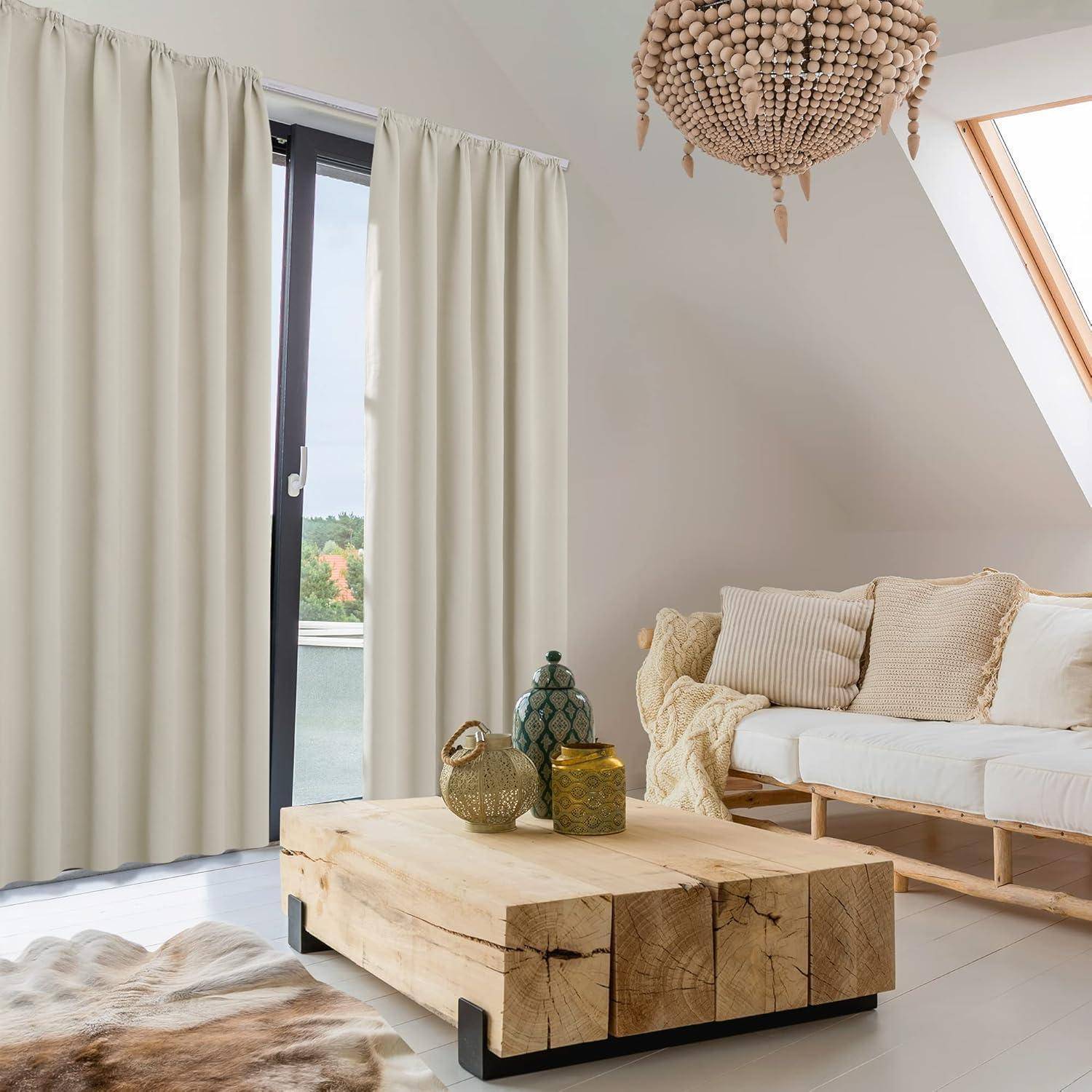Ein heller Wohnraum mit einem großen Fenster, das von hellen Beige-Gardinen verhangen ist, ein Holzkaffeetisch, Cremefarbenes Sofa mit Kissen und ein runder Kronleuchter.