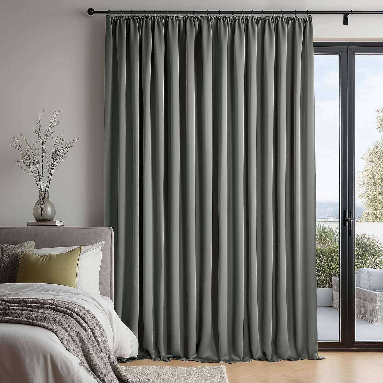 Ein Schlafzimmer mit einem ordentlich gemachten Bett, einer grünen Decke und Kissen. Graue Vorhänge verdecken ein großes Fenster, mit einem Blick auf Grünflächen draußen.
