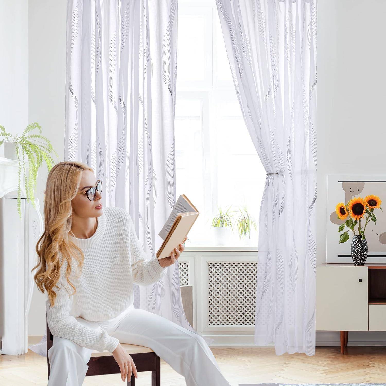 Eine Frau in einem weißen Pullover sitzt in einem hellen Raum und liest ein Buch. Sonnenlicht strömt durch transparente Vorhänge, und eine Topfpflanze steht in der Nähe.