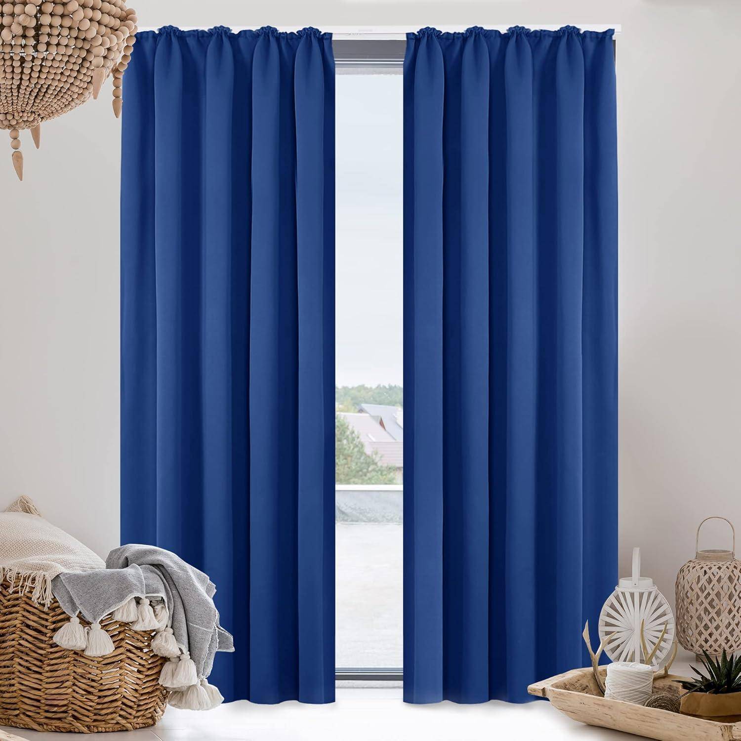 Ein Raum mit einem großen Fenster, umrahmt von blauen Vorhängen, dekoriert mit neutralfarbenen Textilien und einer Topfpflanze, der einen Blick in die Ferne freigibt.