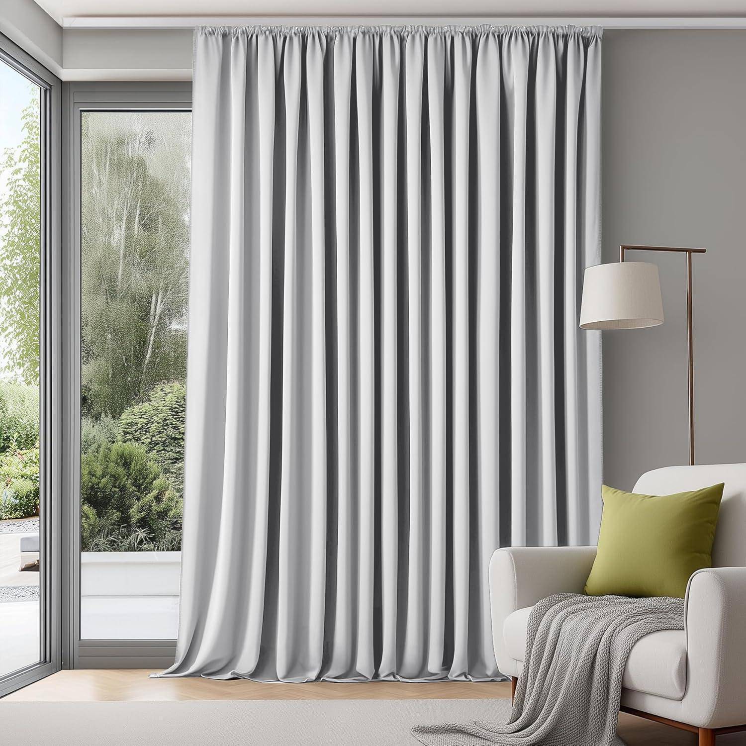 Ein gemütliches Wohnzimmer mit einem großen Fenster, das von weißen Gardinen verhängt ist, einem cremefarbenen Sessel, einem grünen Kissen und einer Stehlampe in der Ecke.