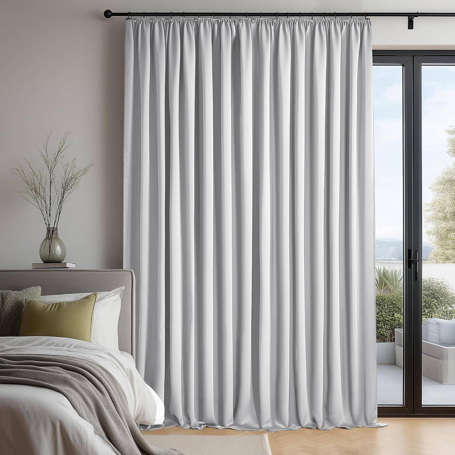 Ein Schlafzimmer mit einem ordentlich gemachten Bett, weißen Vorhängen, einer kleinen Vase auf dem Nachttisch und einem Blick auf Bäume durch eine Glastür.