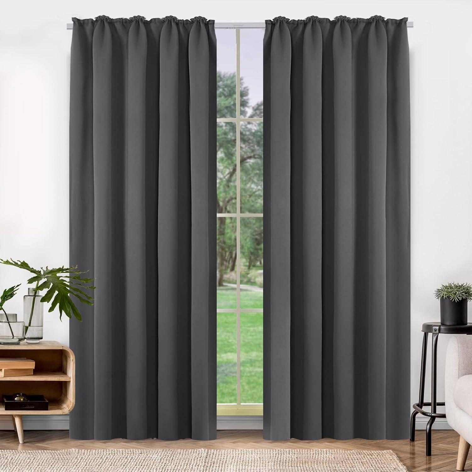 Ein Fenster mit grauen Vorhängen, die an beiden Seiten zugezogen sind und einen bewaldeten Außenblick freigeben. Im Innenraum befinden sich Zimmerpflanzen und ein kleines Holzregal.