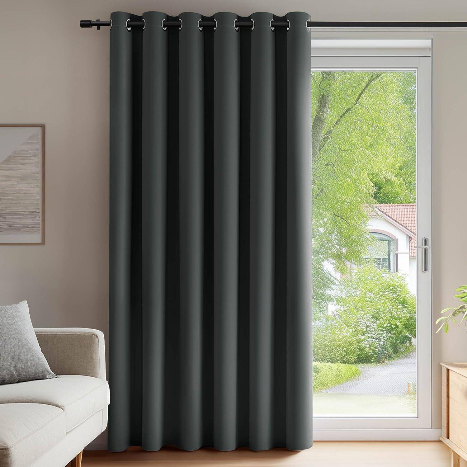Ein modernes Wohnzimmer verfügt über ein großes Fenster mit dunkelgrauen Vorhängen, die geöffnet sind, um natürliches Licht hereinzulassen, und einen Blick auf einen Garten mit grünem Blattwerk bieten.