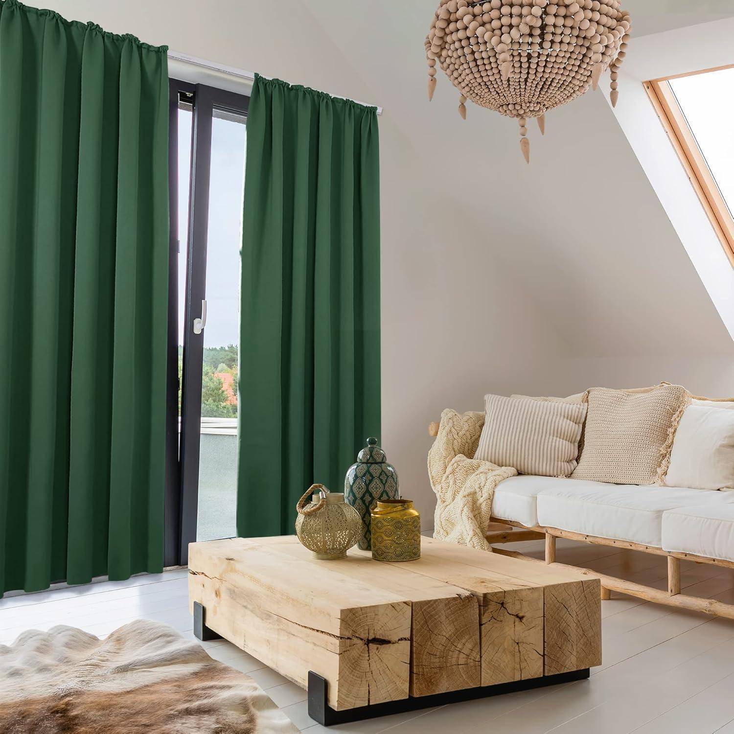 Ein gemütliches Wohnzimmer mit grünen Vorhängen, einem cremefarbenen Sofa, einem Holzkaffeetisch und einem Oberlicht. Eine Pendelleuchte und Dekoration verleihen Wärme.