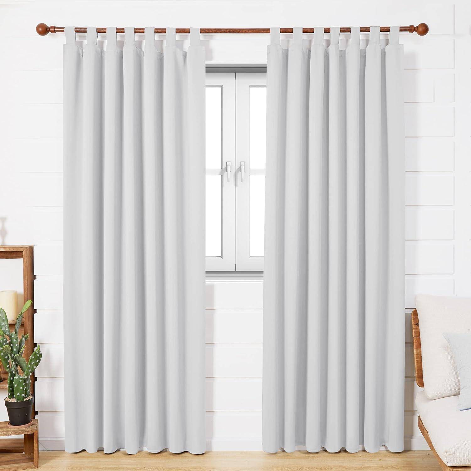 Weiße Vorhänge sind ordentlich an einer Stange aufgehängt und rahmen ein Fenster in einem hellen Raum. Eine kleine Pflanze ist im linken Vordergrund sichtbar.