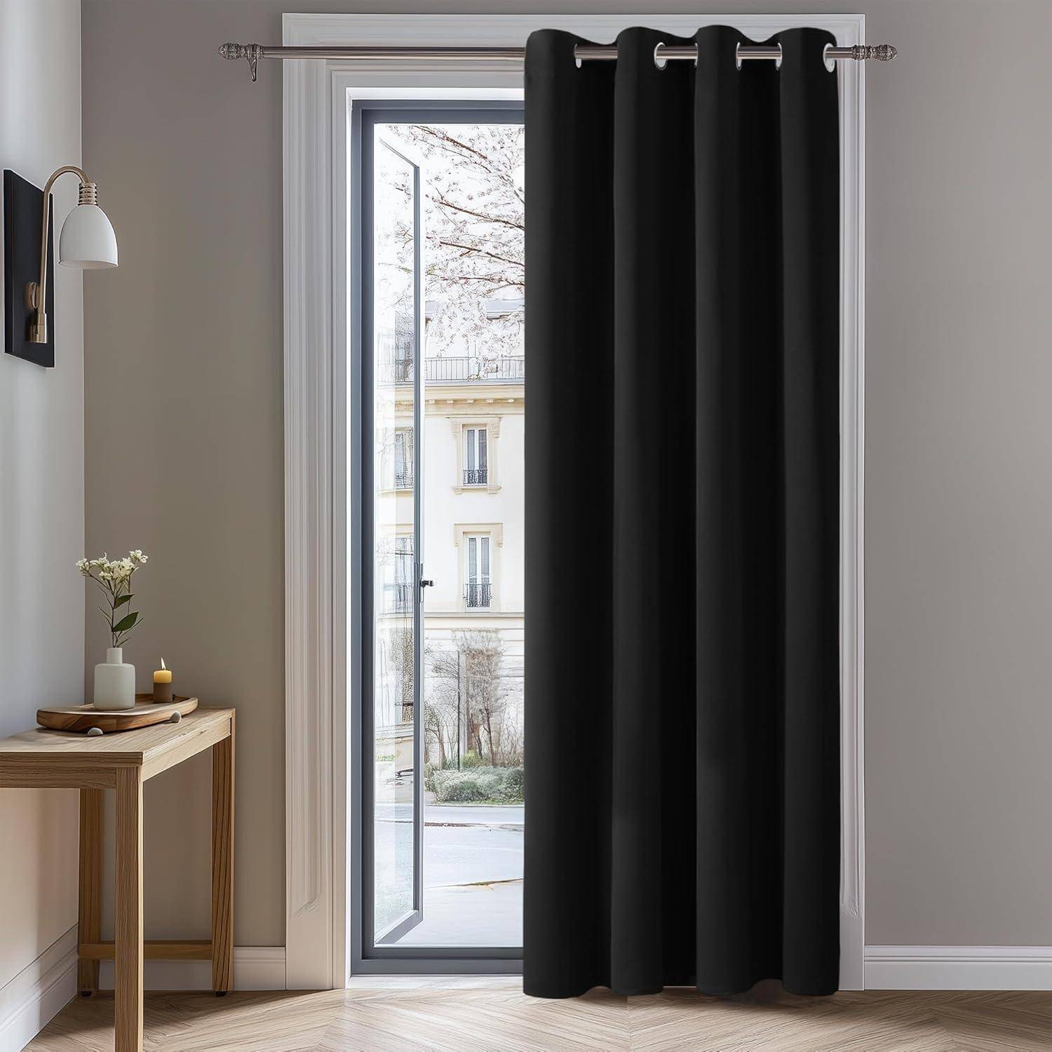 Eine Glastür in einem Raum führt zu einer Außenansicht von Gebäuden und Bäumen. Die Tür ist von schwarzen Vorhängen umrahmt, mit einem kleinen Tisch in der Nähe.