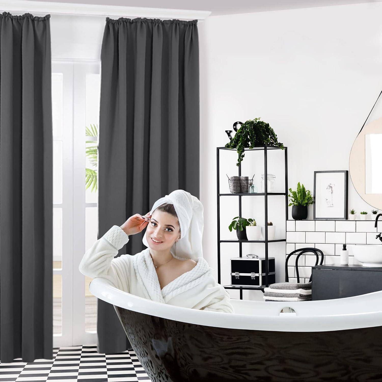 Eine Frau in einem Bademantel mit einem Handtuch auf dem Kopf steht neben einer Badewanne mit Löwenfüßen in einem modernen Badezimmer. Der Raum hat Pflanzen und einen Spiegel.