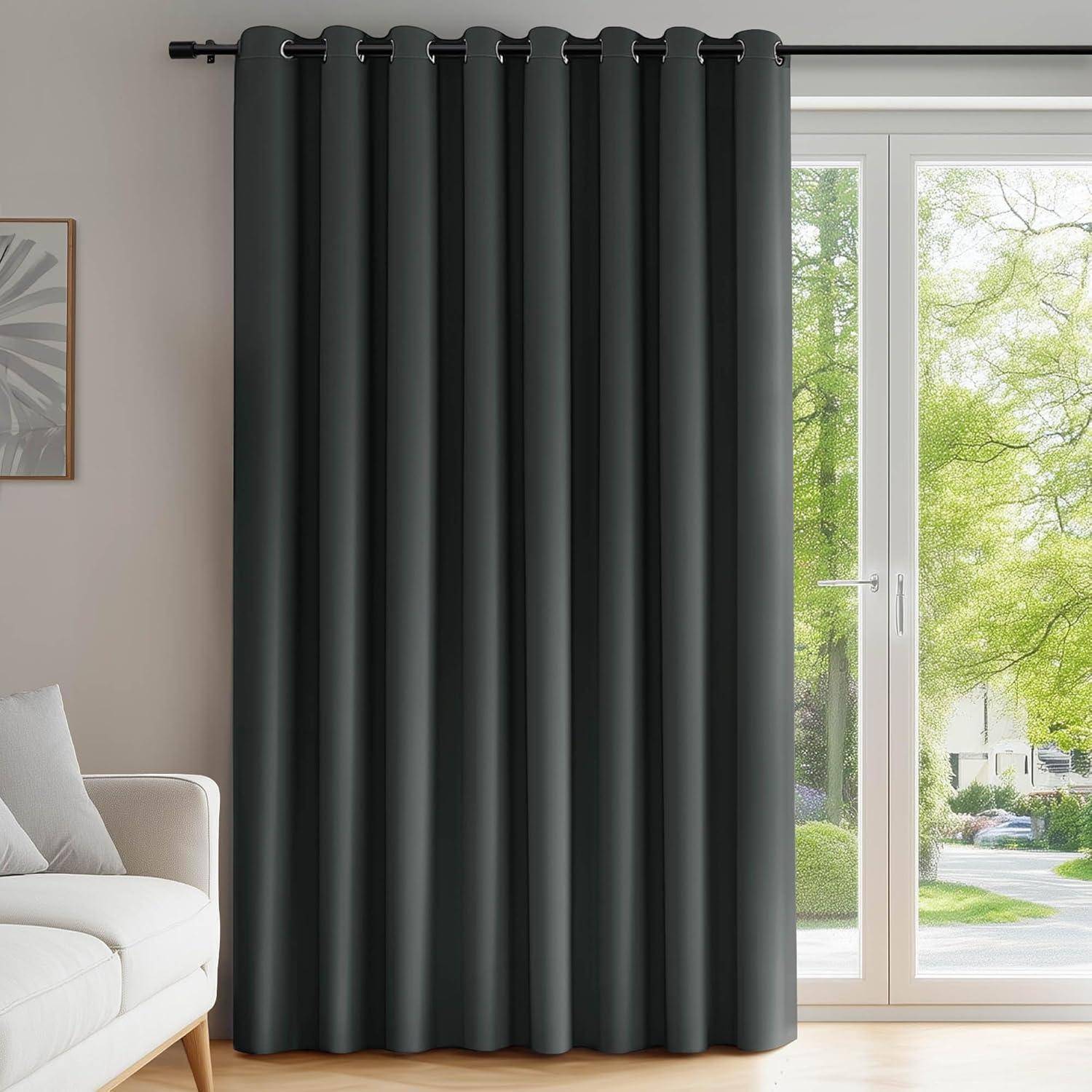 Dunkelgraue Verdunkelungsvorhänge, die vor einem großen Fenster mit Blick auf einen grünen Garten hängen, neben einem Teil eines Sofas auf der linken Seite.