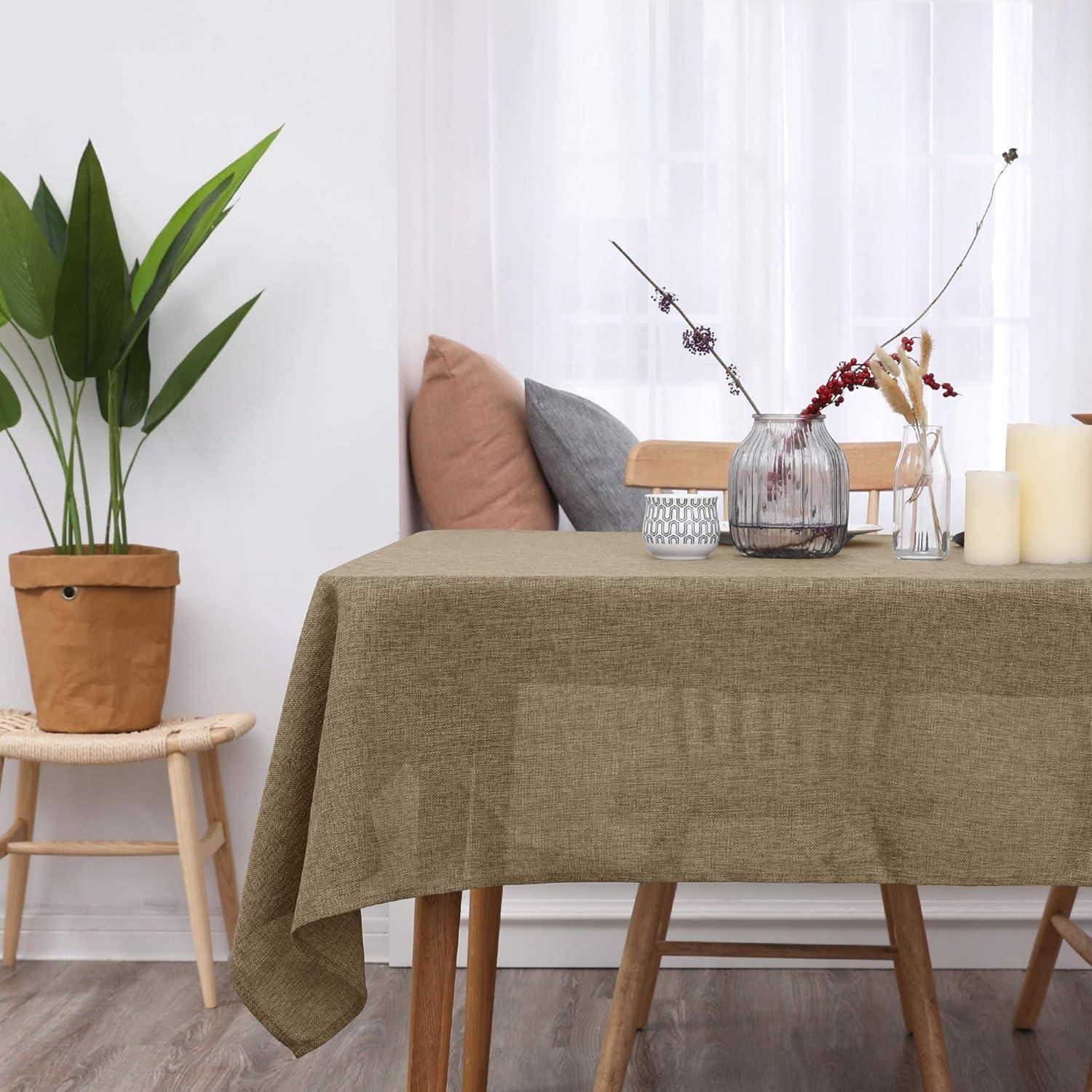 Ein Esstisch, bedeckt mit einer beigen Tischdecke, geschmückt mit einer Vase roter Blumen, einer Kerze und einer kleinen Pflanze auf einem Hocker in der Nähe.