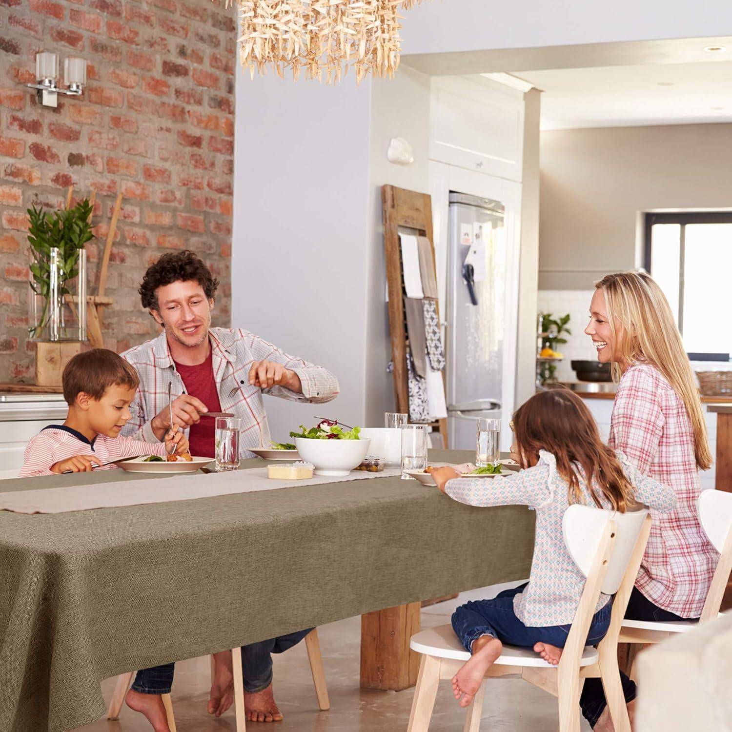 Eine Familie mit vier Personen sitzt um einen Esstisch und teilt eine Mahlzeit, lächelt und lacht gemeinsam in einer gemütlichen, hell erleuchteten Küchenumgebung.