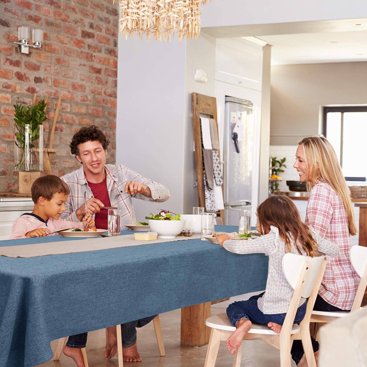 Eine Familie mit vier Personen sitzt an einem Esstisch, der mit Tellern und Essen gedeckt ist. Sie wirken aufgeschlossen und glücklich, während sie gemeinsam in einer gemütlichen Küche eine Mahlzeit teilen.