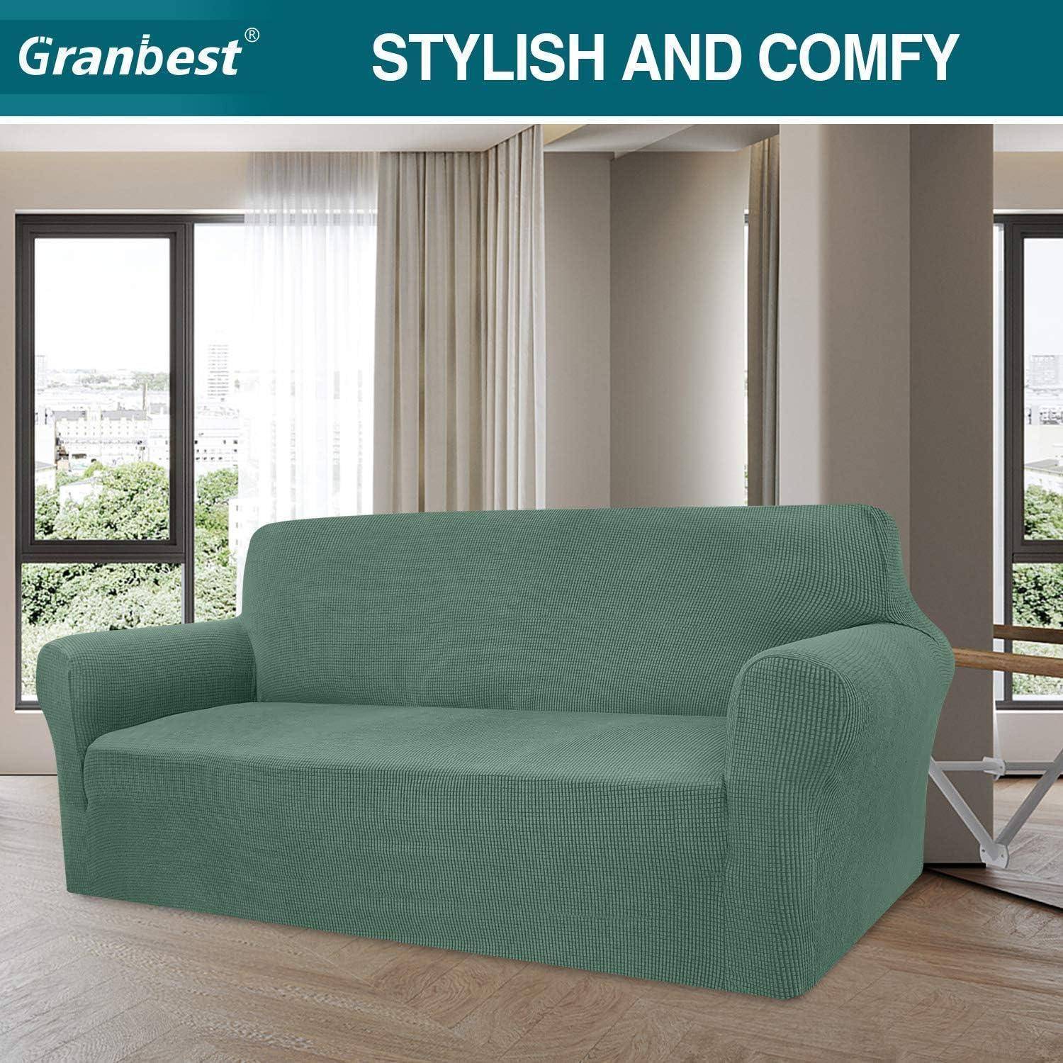 Ein modernes Wohnzimmer präsentiert ein Sofa in Entenblau mit einem passgenau bezogenen Überzug, das vor großen Fenstern mit weißen Vorhängen platziert ist, unter dem Text ‚Stilvoll und gemütlich'.
