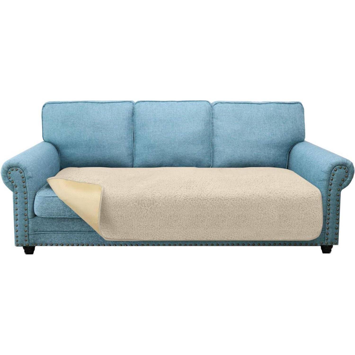 Eine blaue Couch mit drei Kissen ist teilweise von einer beigen, strukturierten Decke auf dem Sitzbezirk bedeckt, was Komfort und Stil suggeriert.