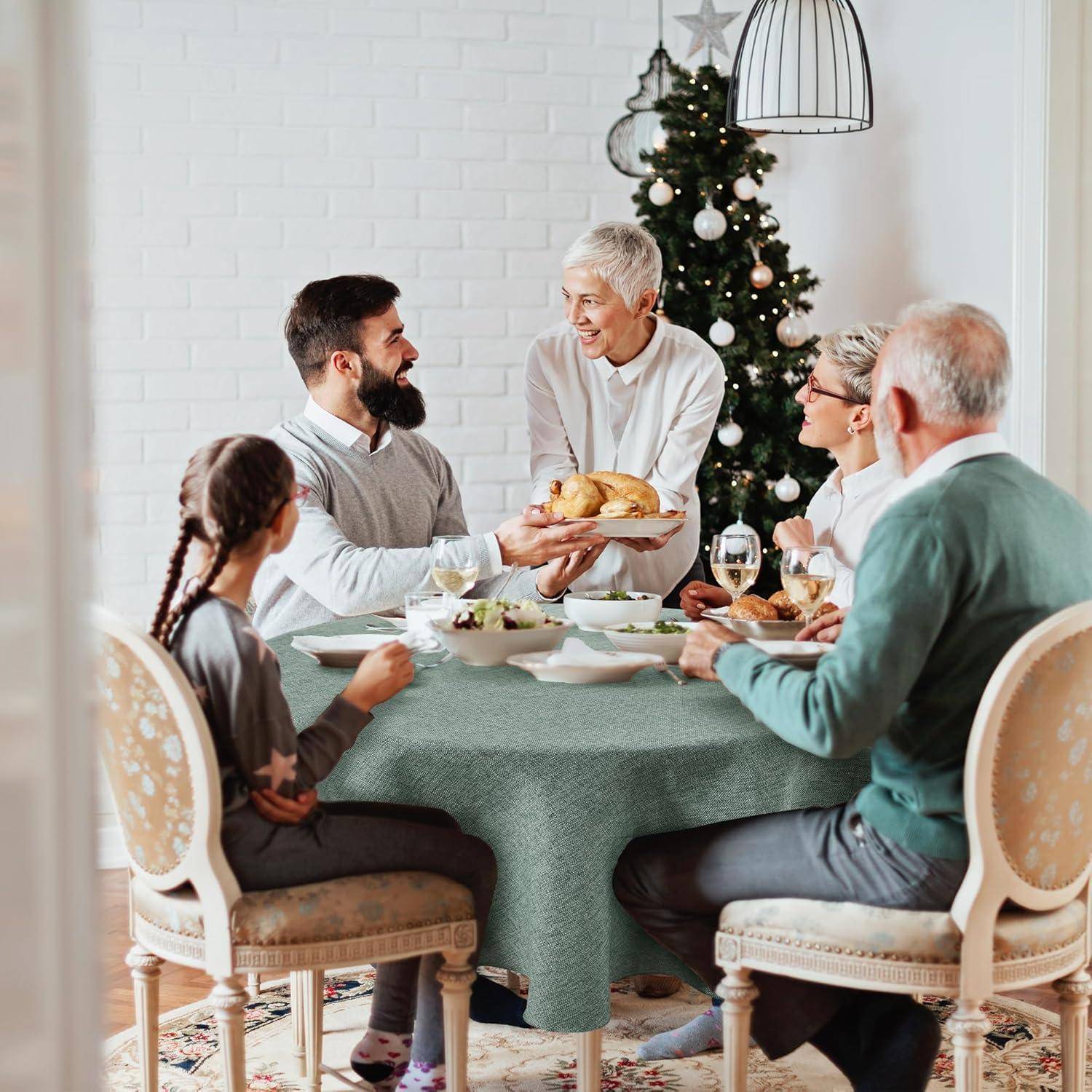 Familie versammelt um einen Esstisch, die Mahlzeit wird neben einem Weihnachtsbaum geteilt. Eine Person steht auf und hält ein gebratenes Huhn, bereit zum Servieren.