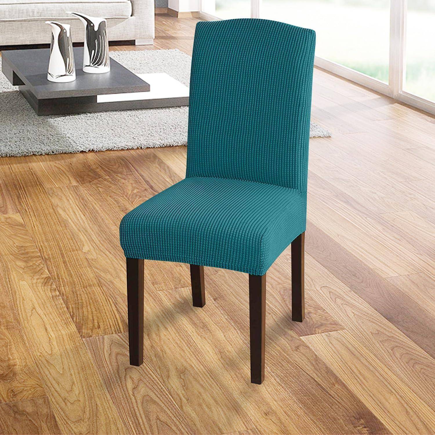 Ein petrolblau gepolsterter Essstuhl mit schwarzen Beinen auf einem Holzboden in einer Wohnzimmereinrichtung, mit einem Couchtisch und Deko im Hintergrund.