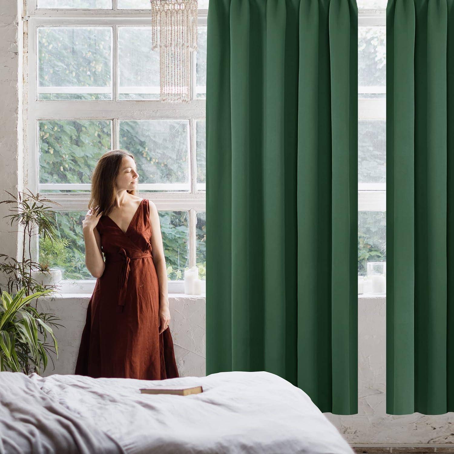 Eine Frau in einem roten Kleid steht neben einem großen Fenster mit grünen Vorhängen und blickt nach draußen. Zimmerpflanzen und weiches natürliches Licht erzeugen eine ruhige Atmosphäre.