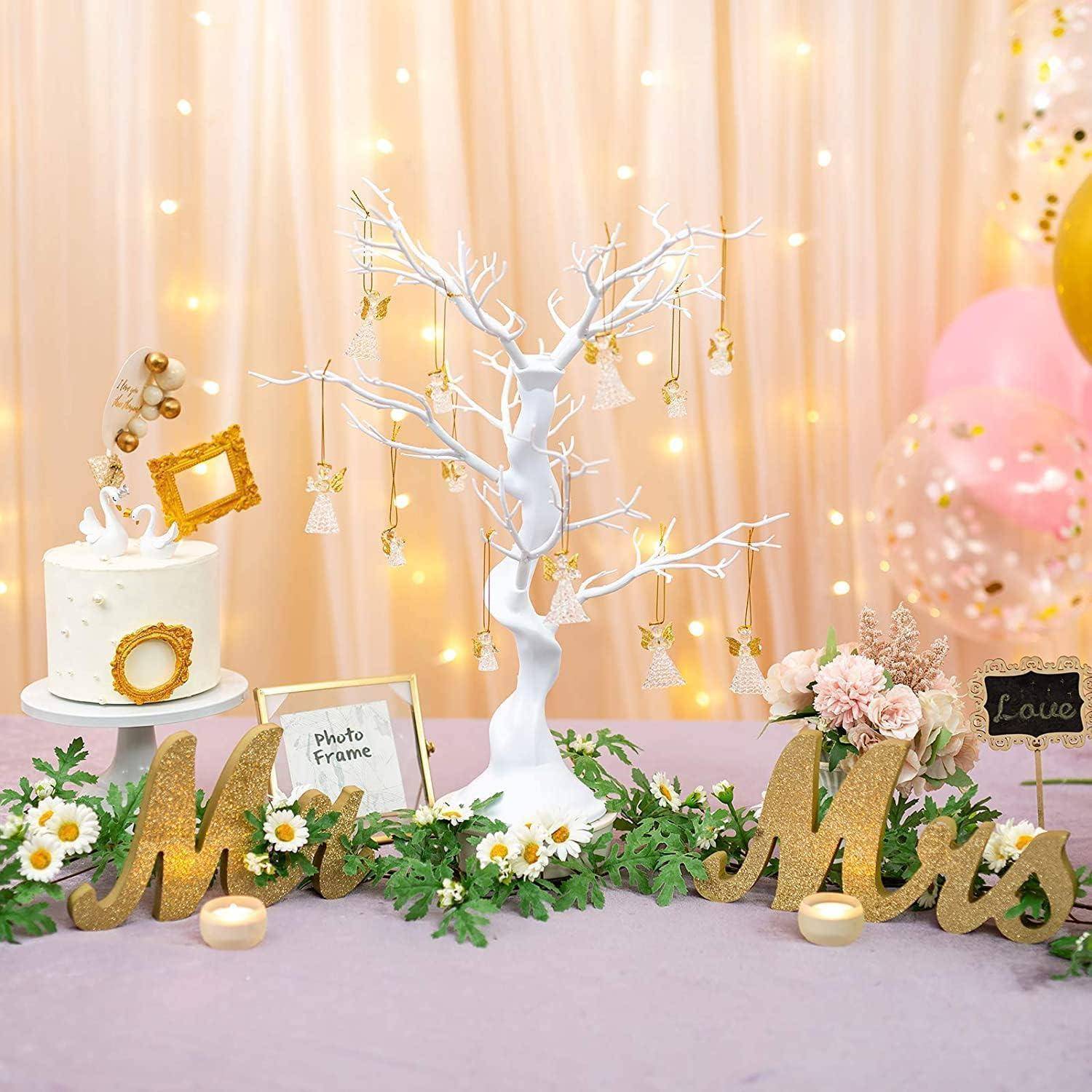 Ein dekorativer Hochzeitstisch mit einer Torte, einem weißen Baumzenterstück und 'Mr & Mrs' Buchstaben, umgeben von Blumen und kleinen Fotos.