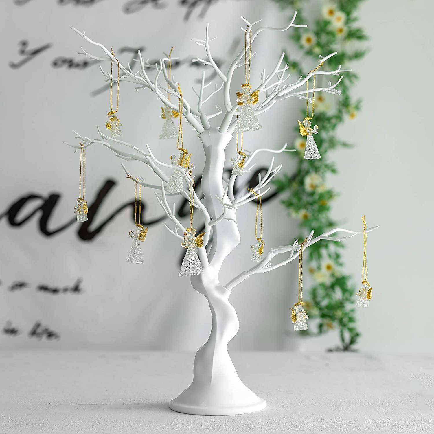 Weißer Deko-Baum mit hängenden Engelsfiguren in einem Raum. Verschwommener Text und florale Akzente im Hintergrund.